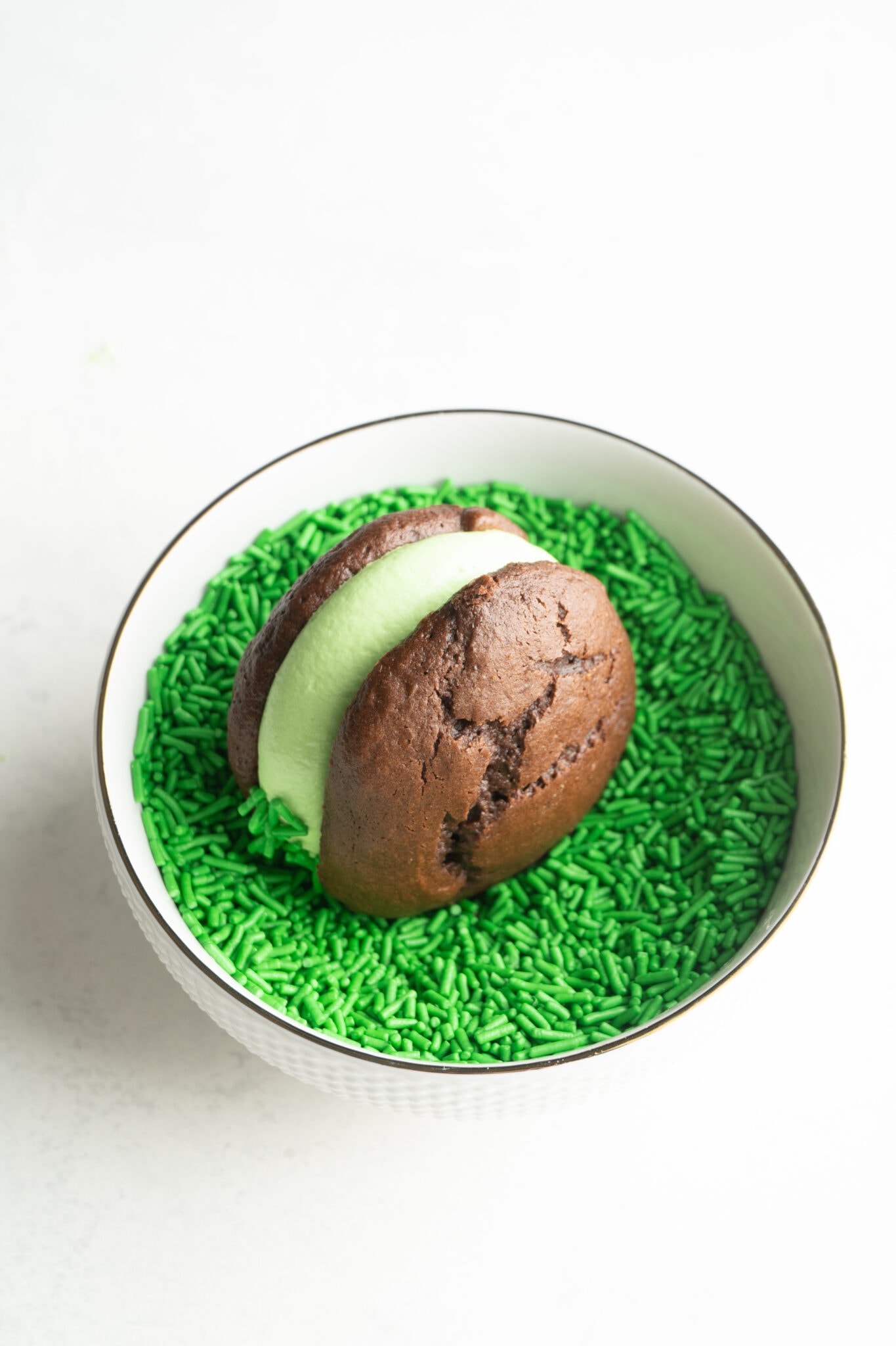 A cake mix whoopie pie being rolled in green sprinkles