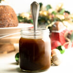 A jar of brandy brown butter sauce with a spoon in the center.