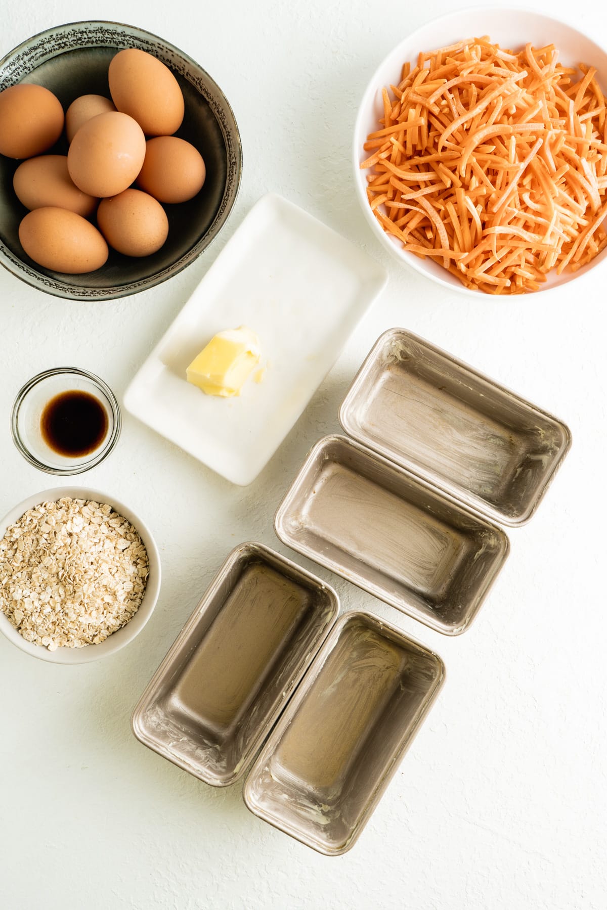 Mini loaf pans greased for a morning bread recipe. The ingredients needed are in individual bowls nearby.