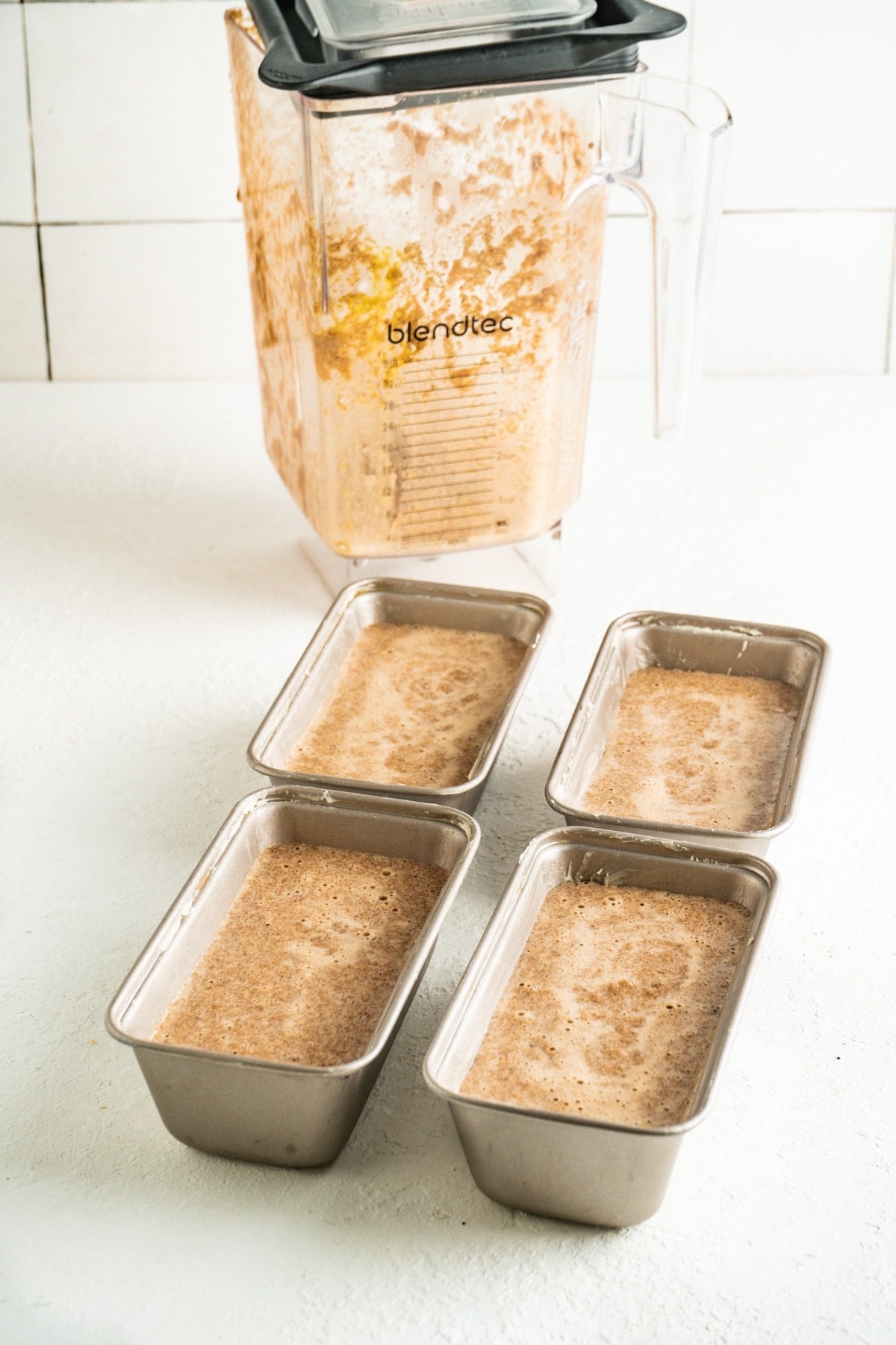 Carrot cake bread batter in mini loaf pans. on a white countertop near a blender.