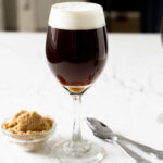 An Irish Coffee beside brown sugar and teaspoons.