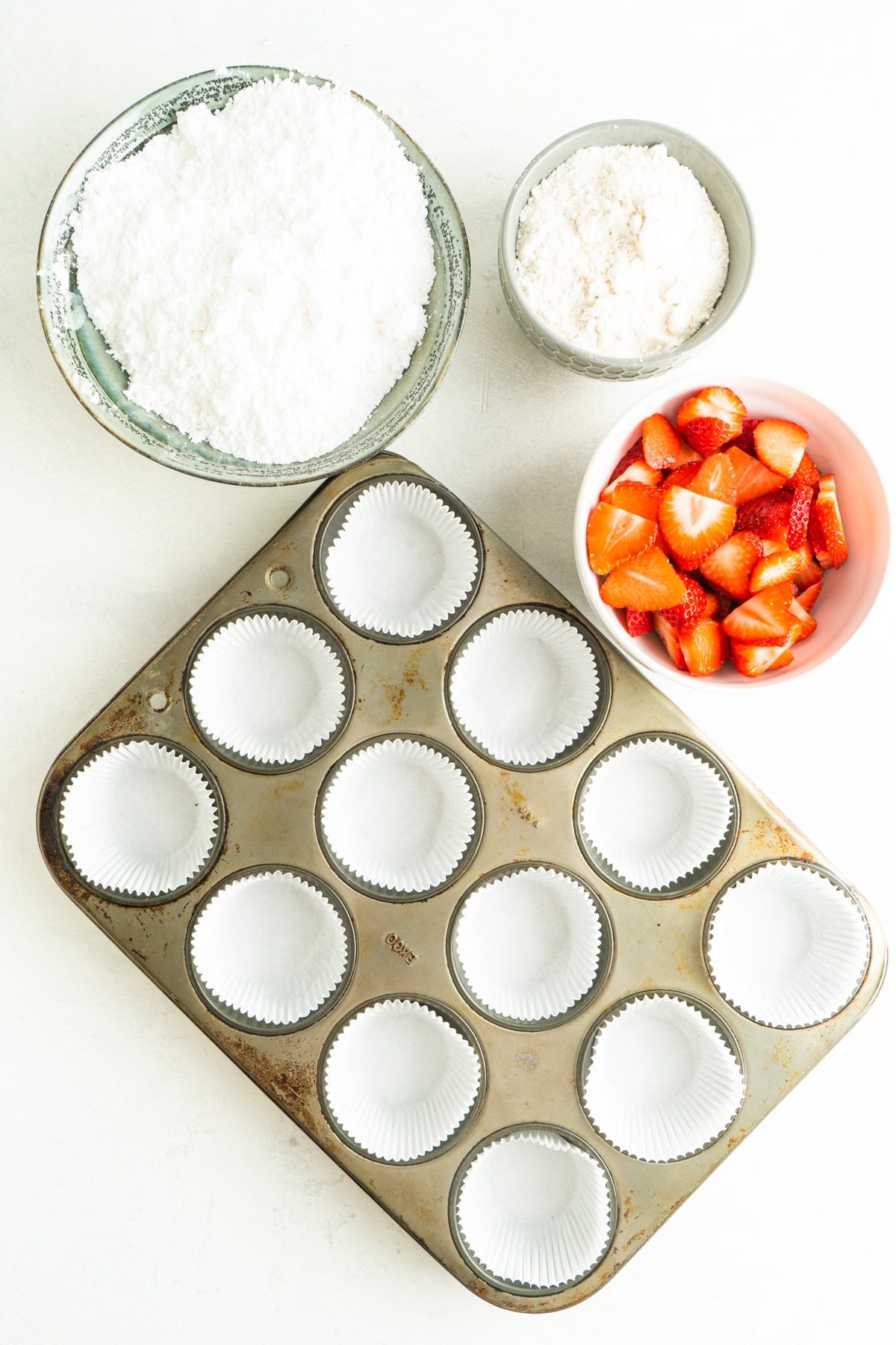 muffin tin lined with cupcake liners and a bowl of strawberries nearby.
