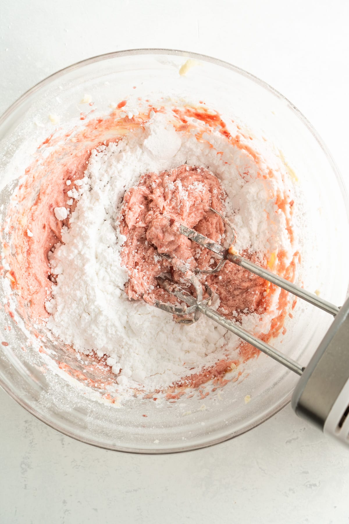 Strawberry butter cream in a bowl with powdered sugar being added