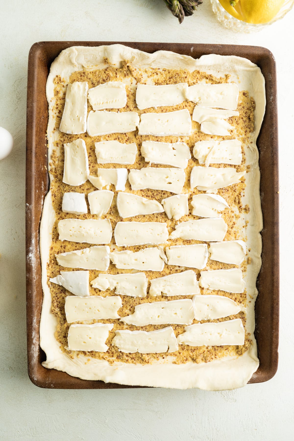 Brie added to a sheet of puff pastry covered in Dijon.