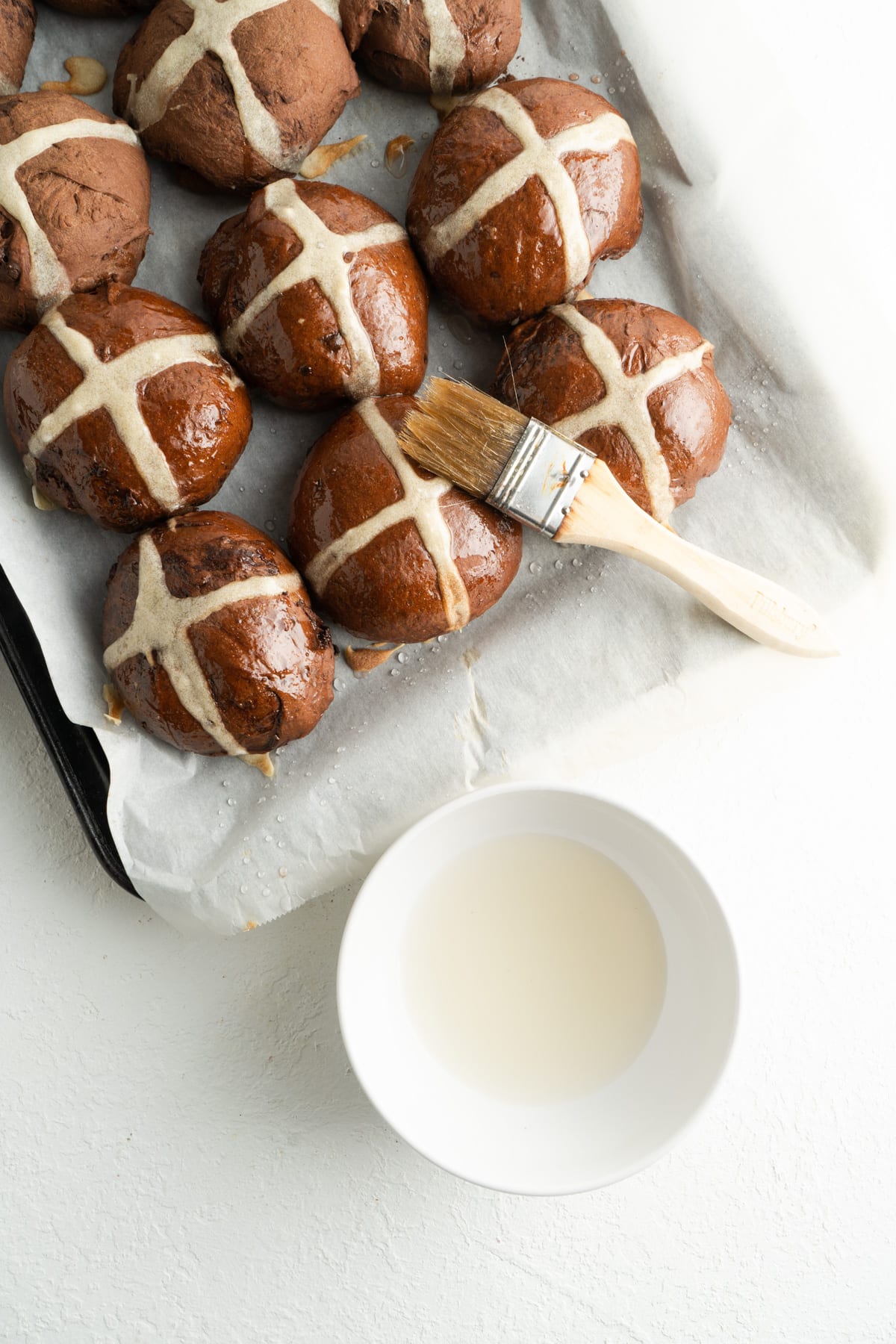 Chocolate easter buns being glazed.