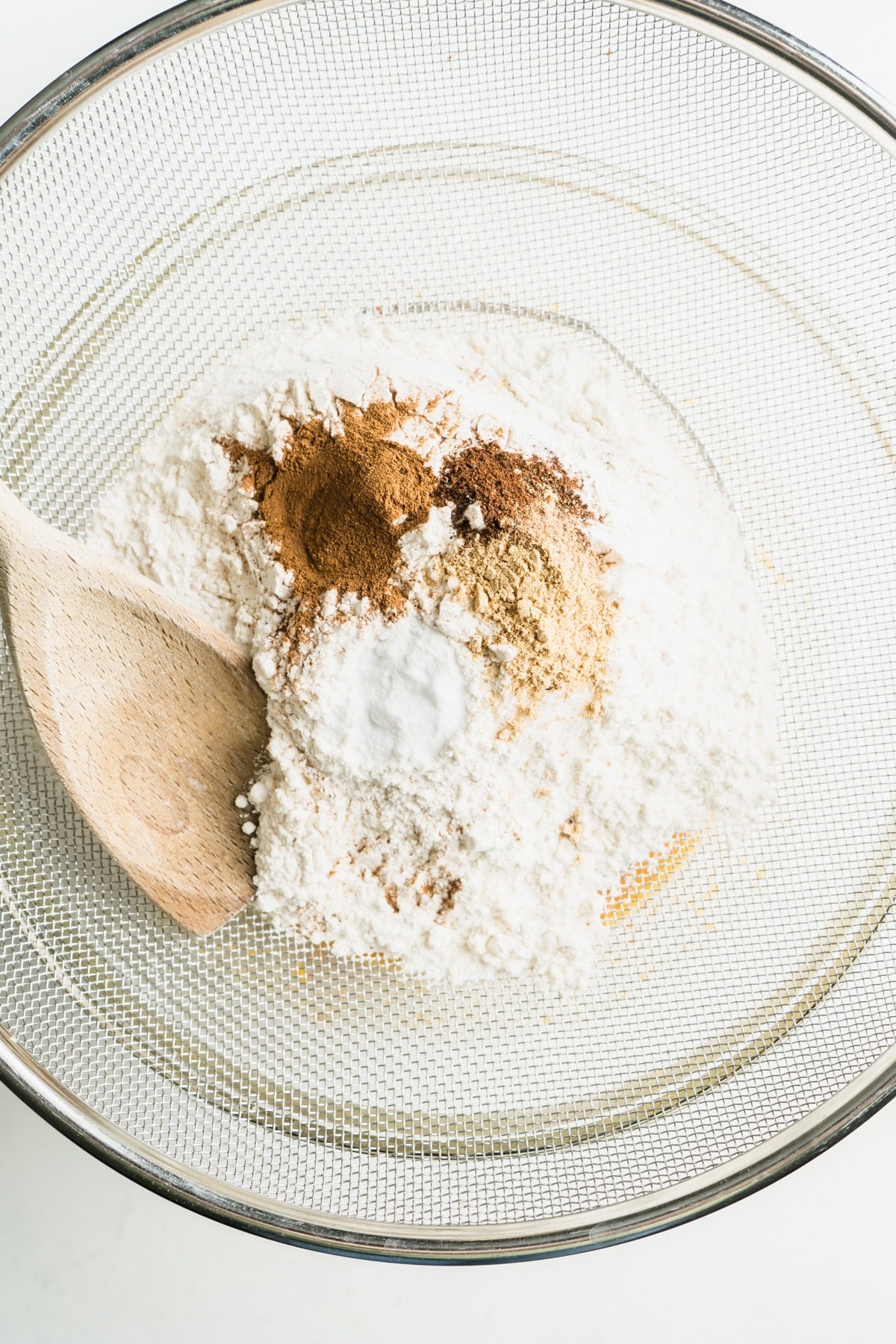 Flour and spices being sifted into a bowl.
