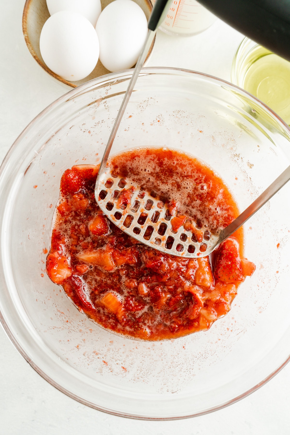 A bowl of strawberries being mashed to release the juices.