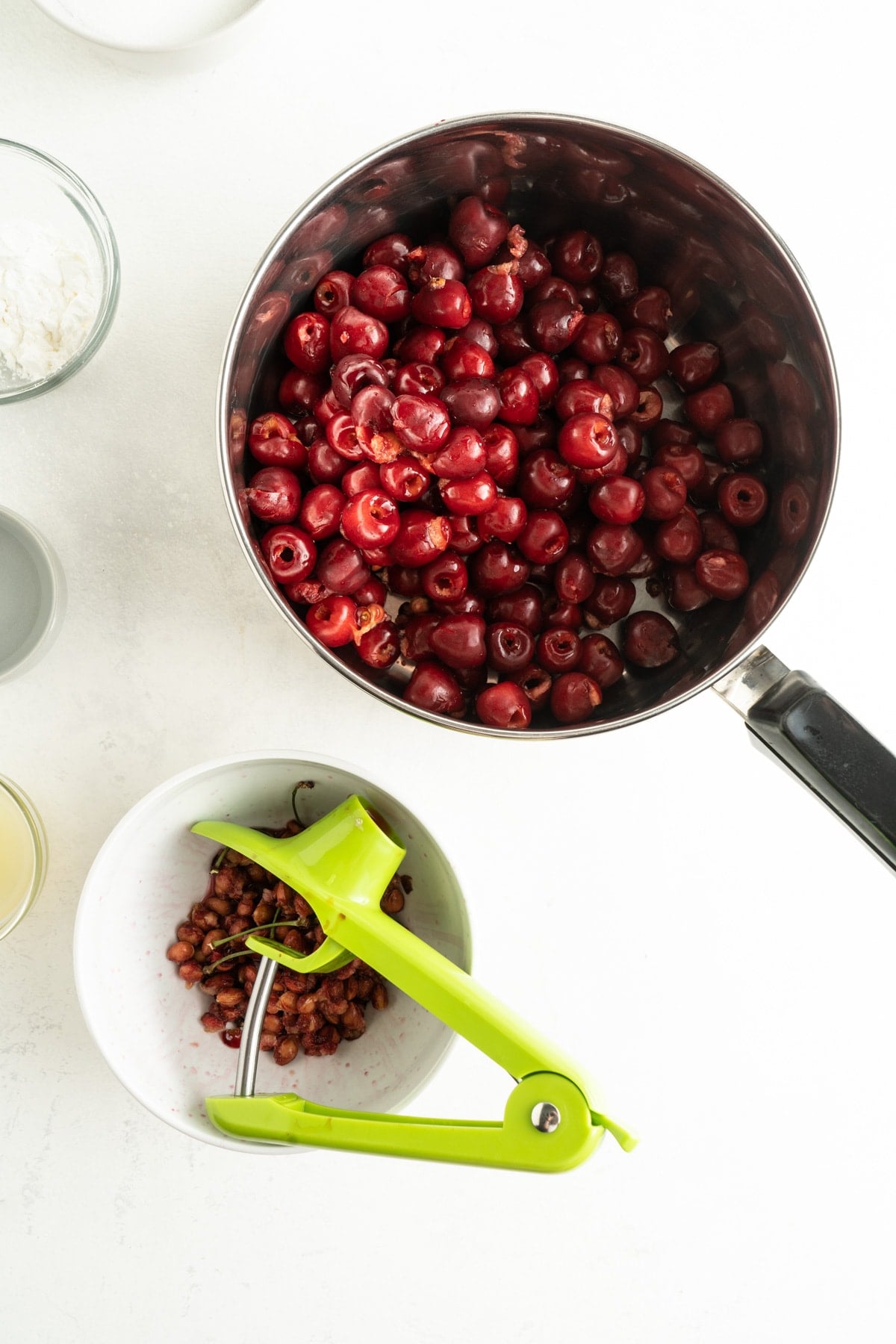 Pitted cherries in a saucepan with a bowl of pits next to it
