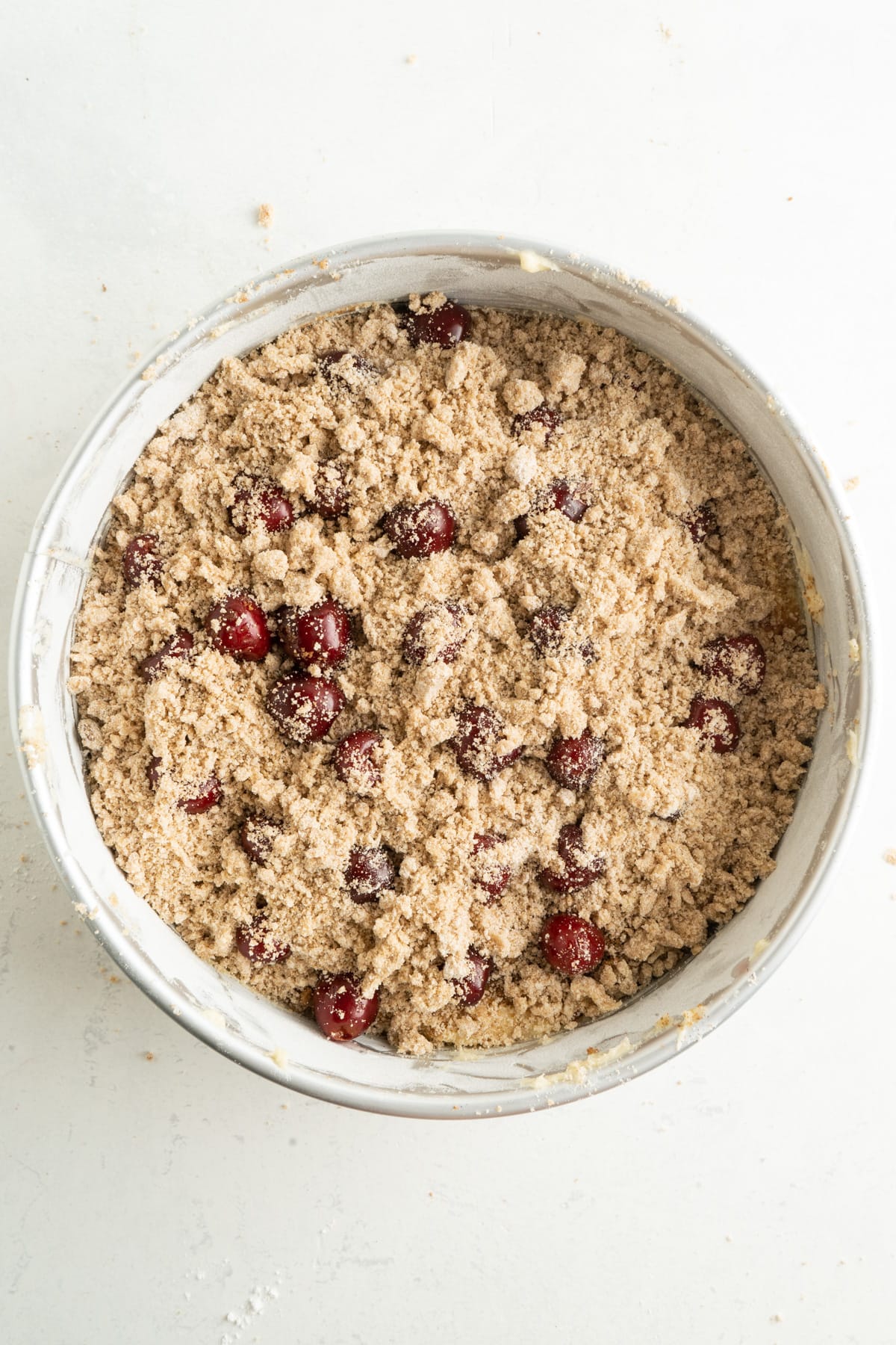 This Cherry Coffee Cake features light, tender layers of cake, a sweet cinnamon swirl, fresh cherries, and an irresistible crumb topping. Crumb topping sprinkled over cherry coffee cake ready to bake