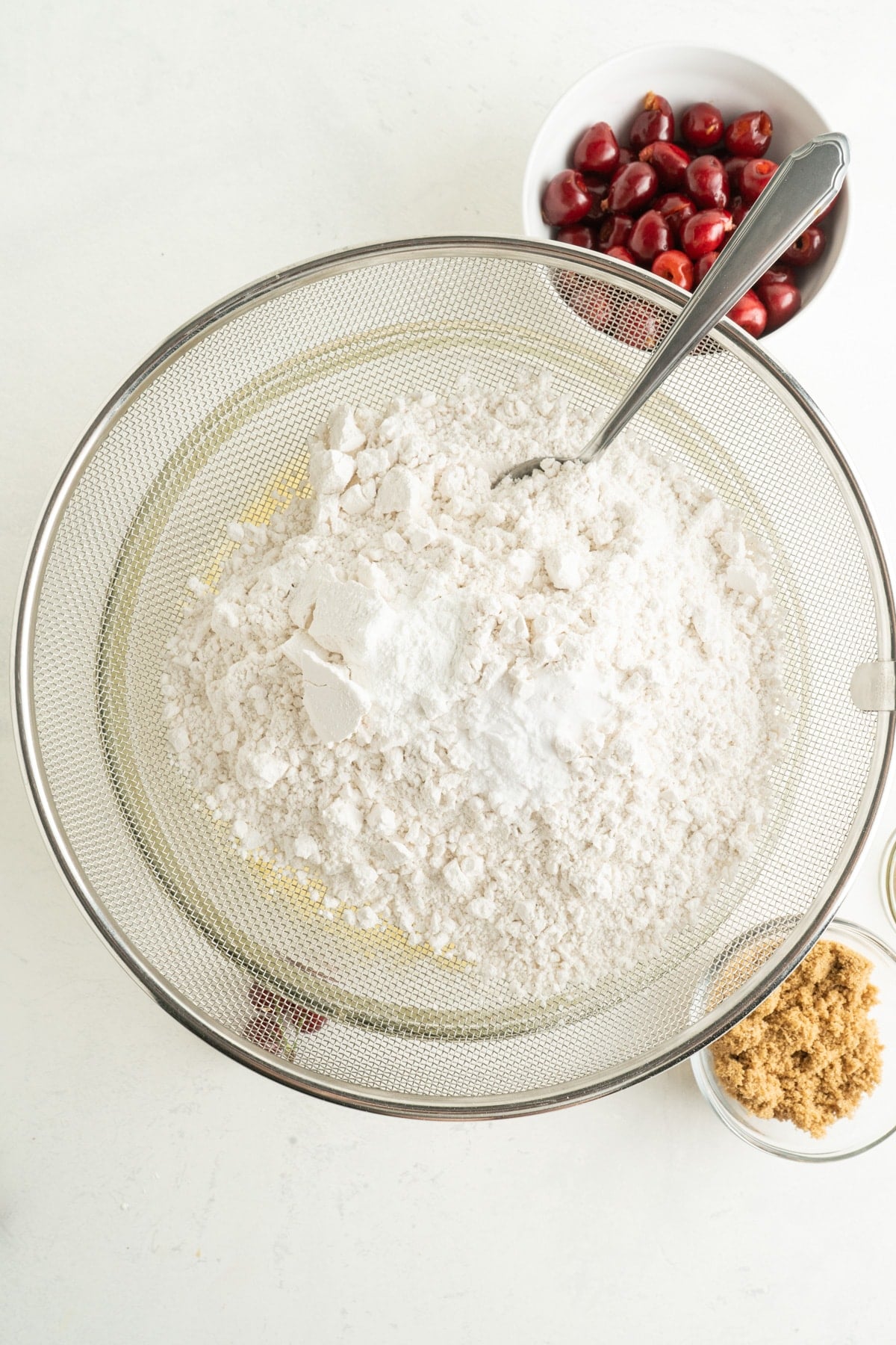 This Cherry Coffee Cake features light, tender layers of cake, a sweet cinnamon swirl, fresh cherries, and an irresistible crumb topping. Dry ingredients in a sieve over a bowl