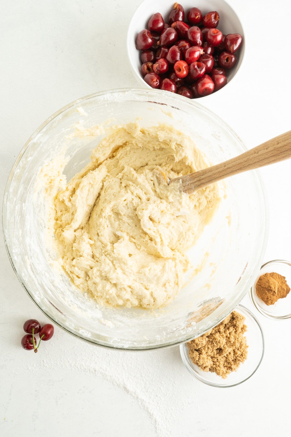 This Cherry Coffee Cake features light, tender layers of cake, a sweet cinnamon swirl, fresh cherries, and an irresistible crumb topping. A wooden spoon mixing coffee cake batter