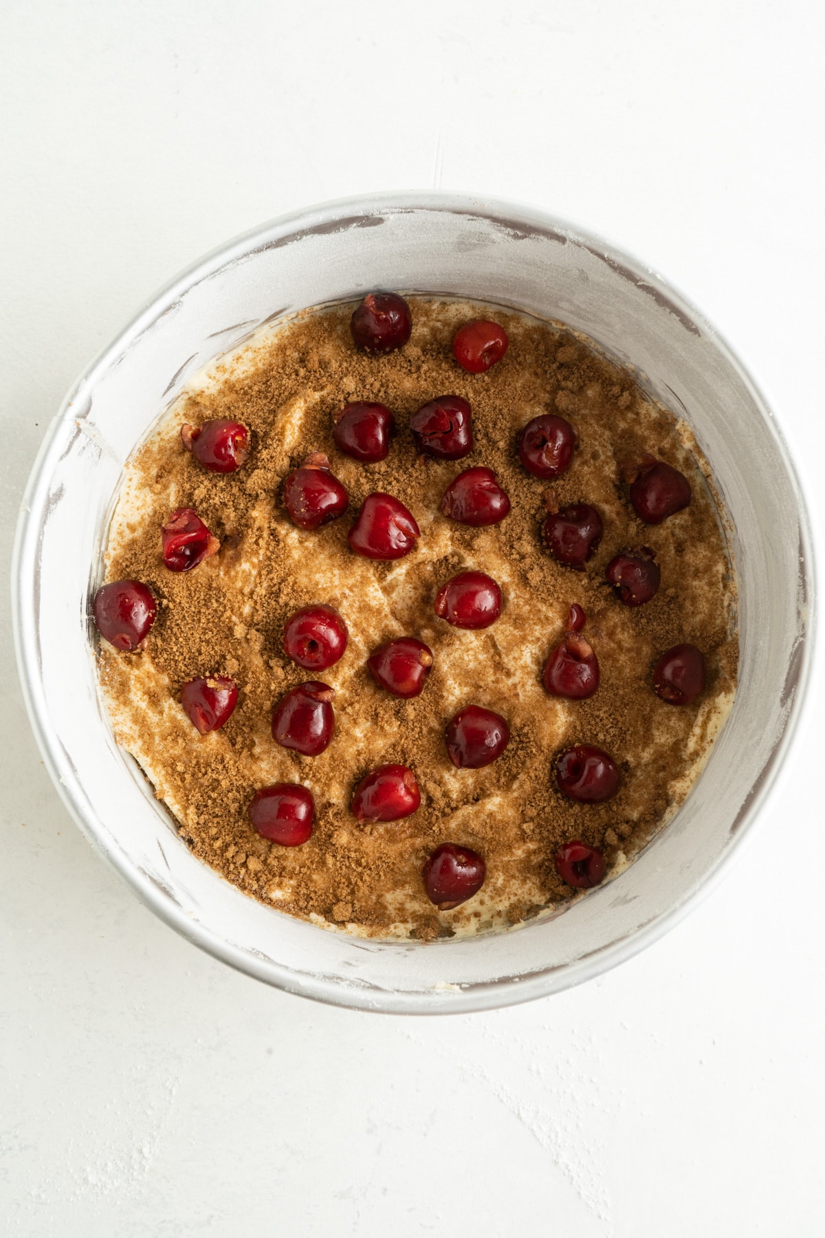 This Cherry Coffee Cake features light, tender layers of cake, a sweet cinnamon swirl, fresh cherries, and an irresistible crumb topping. Cinnamon topping and fresh cherries in a cake pan