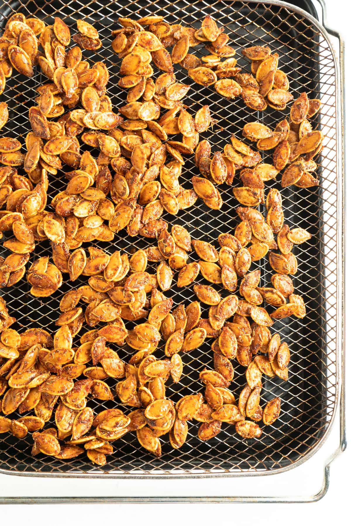 Seasoned pumpkin seeds in an air fryer tray.