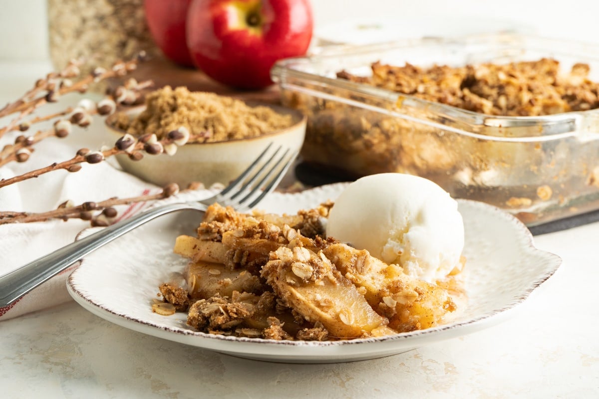 A plate of the best apple crisp with a scoop of ice cream on a table with apples.