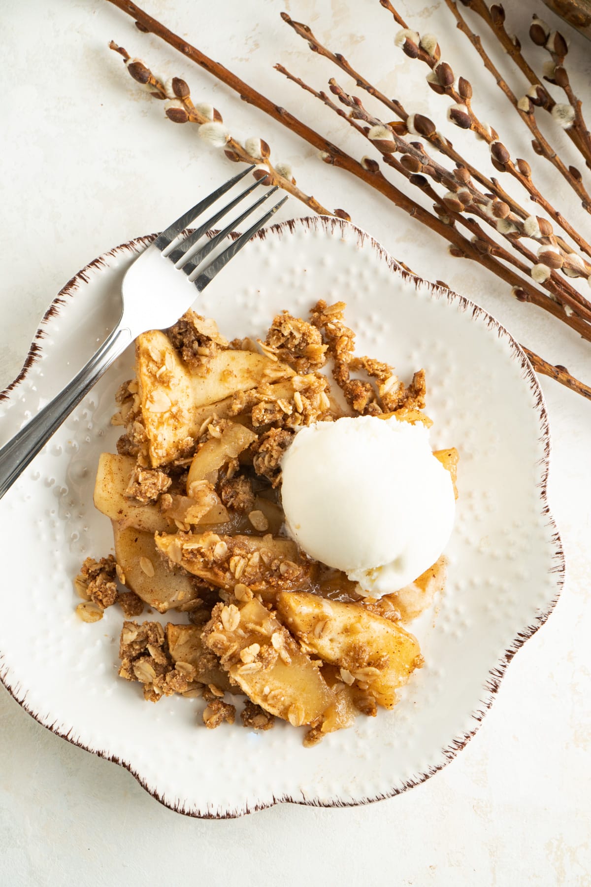 An apple crumble on a plate with a scoop of ice cream and a fork.