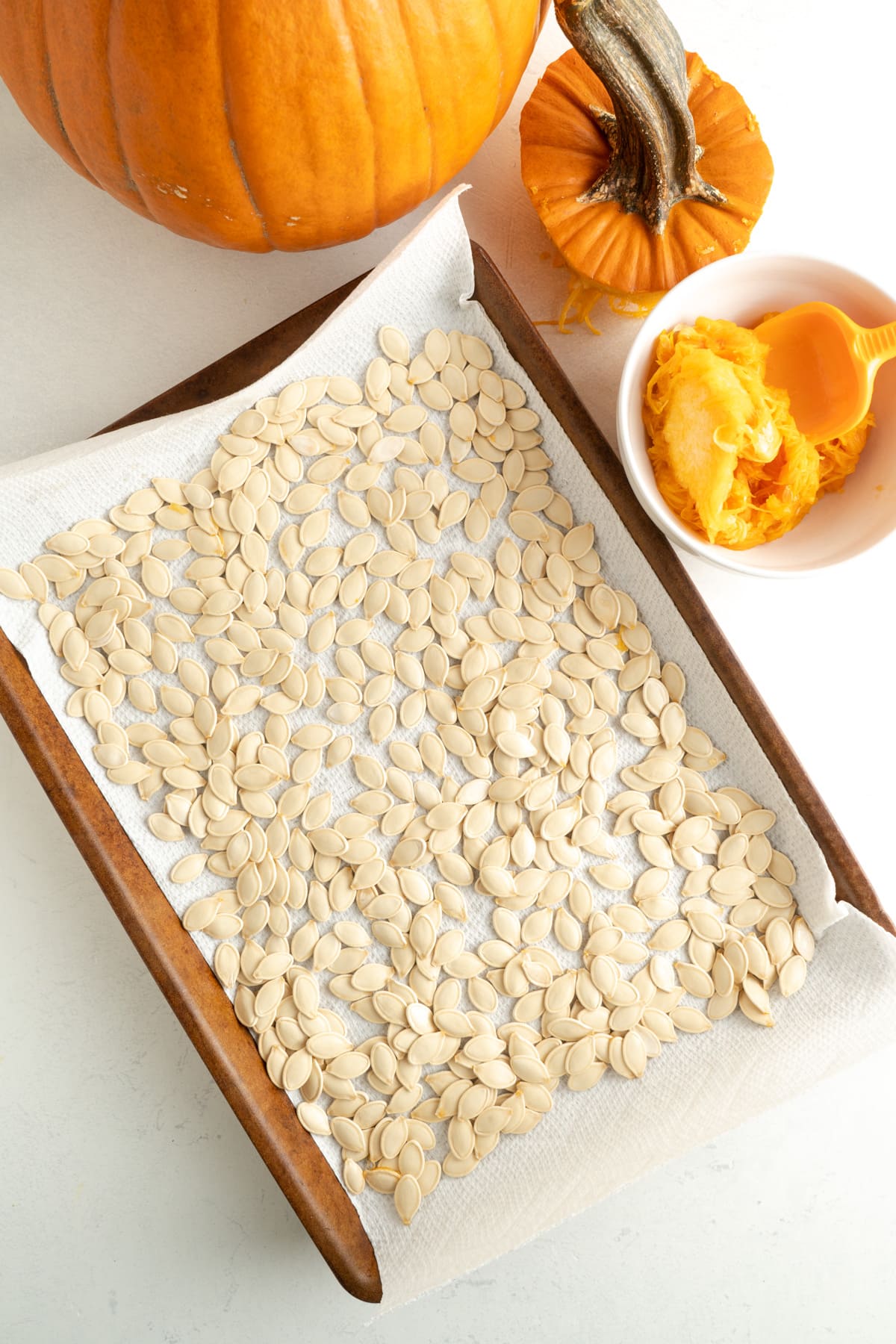 pumpkin seeds drying on a paper towel on top of a baking sheet.