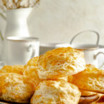 Buttermilk cheese scones on a wooden bowl with mugs of coffee around it.