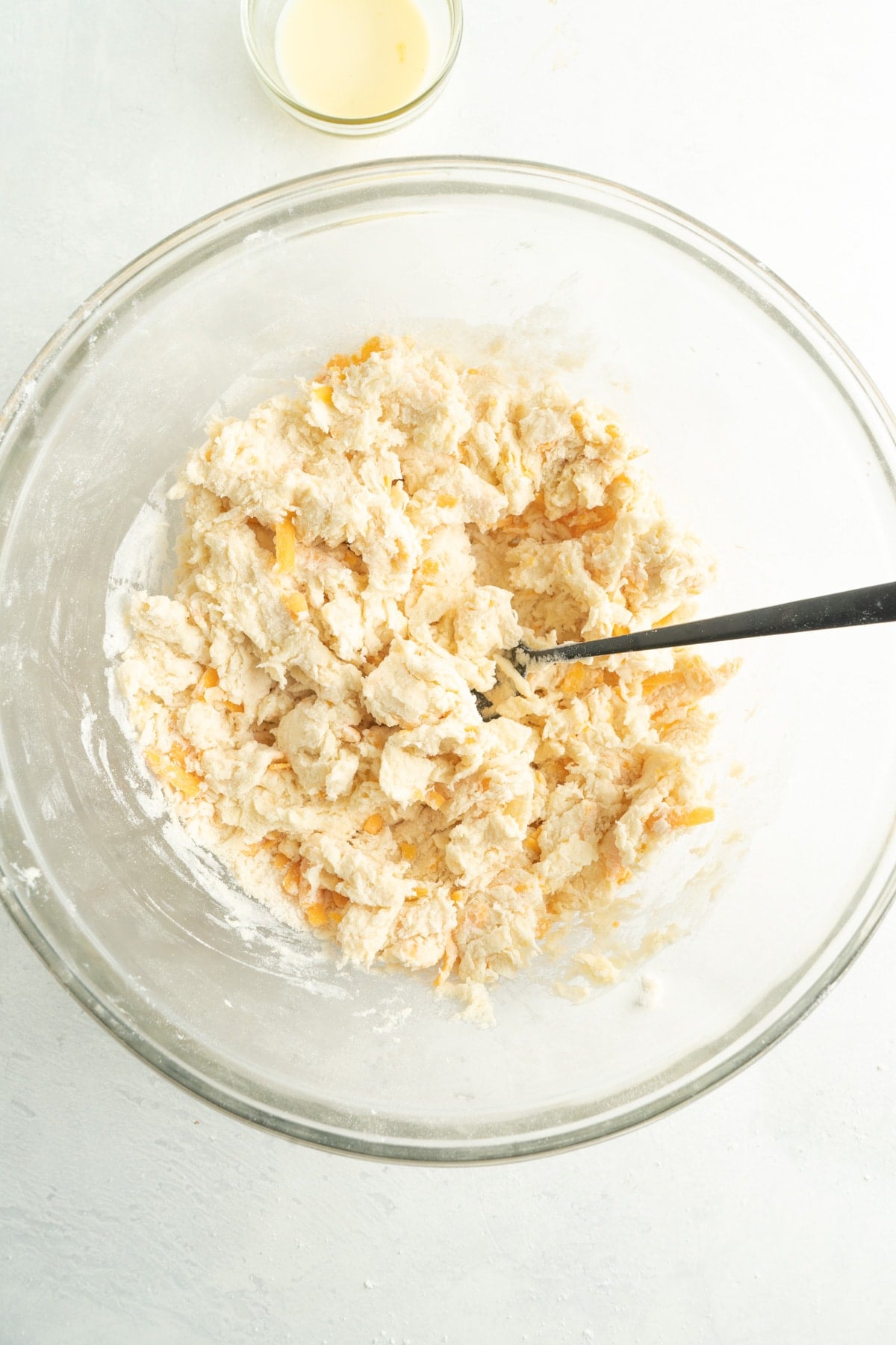 Batter for scones in a glass bowl with a spoon in it.