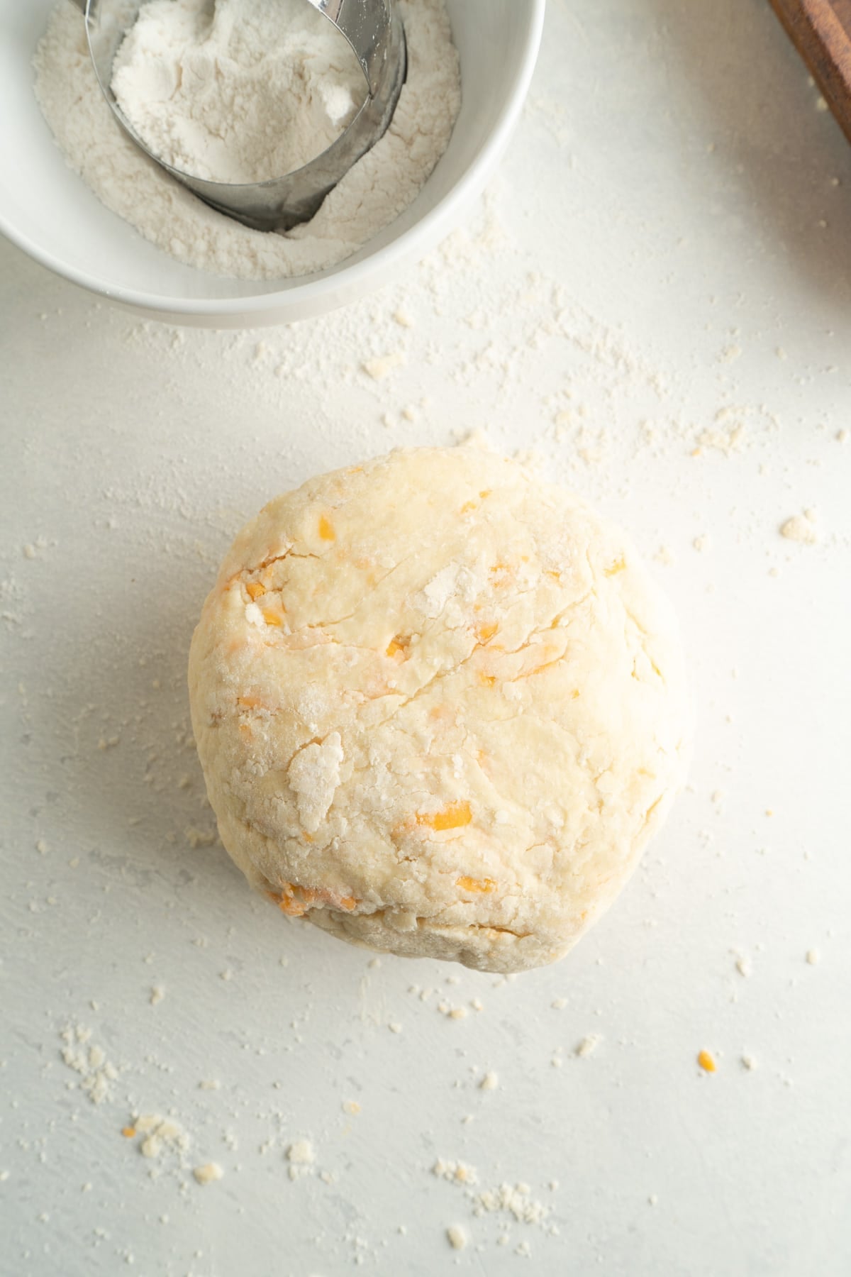 Ball of scone dough with flour in a bowl behind it.