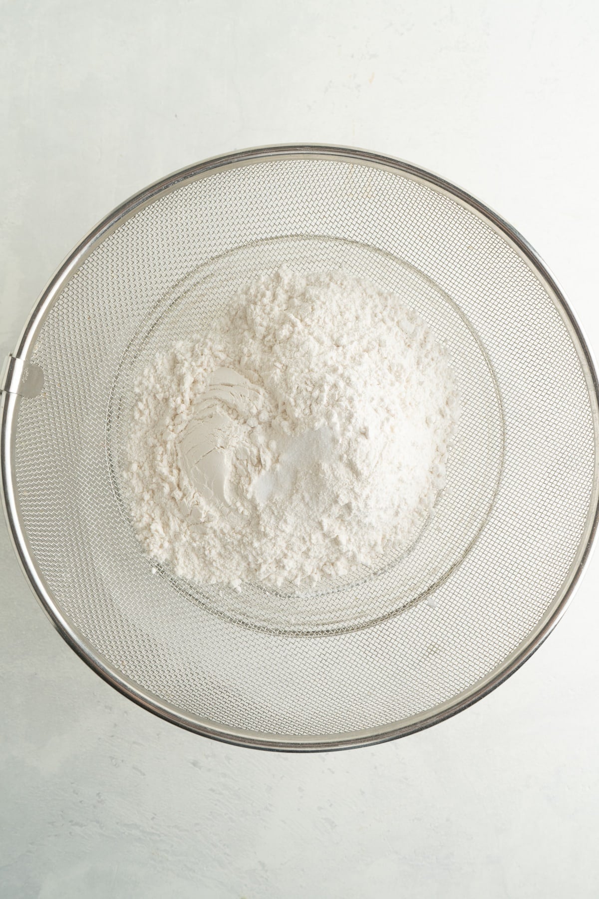 This Italian Pizzelle Cookie Recipe is made with just 7 ingredients. These classic cookies are thin, crispy, and sweet. Flour in a sieve over a large bowl