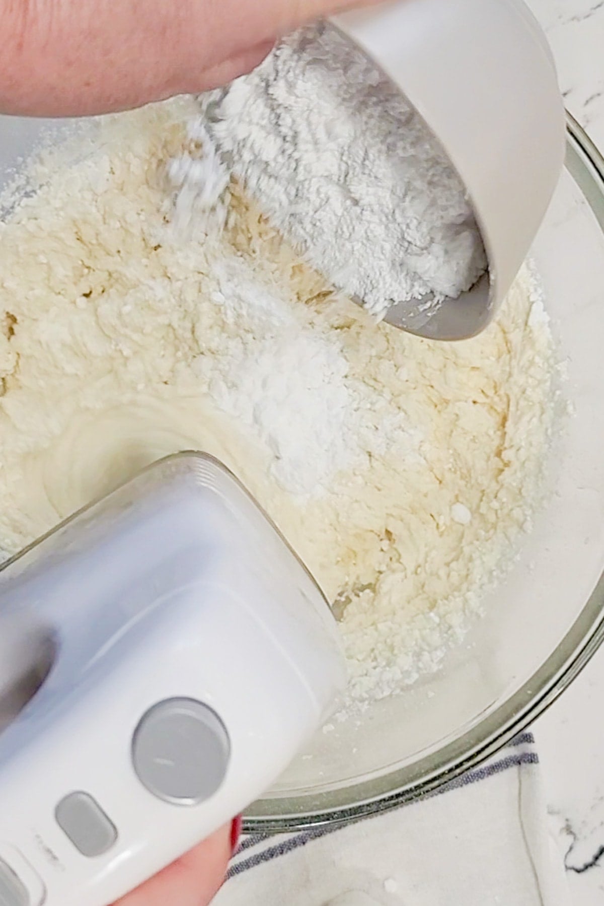 Confectioners sugar being added to a bowl with mascarpone cheese.