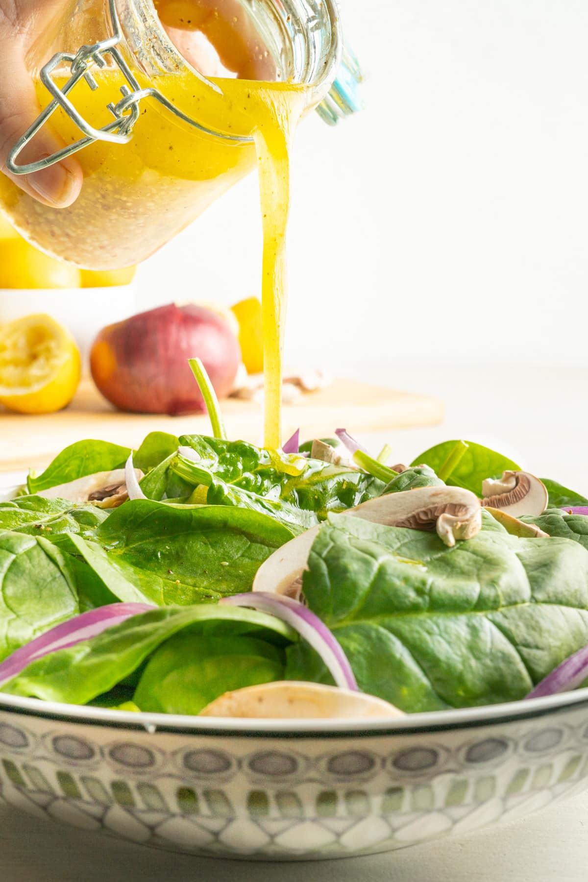 Lemon garlic salad dressing being poured over a spinach salad.