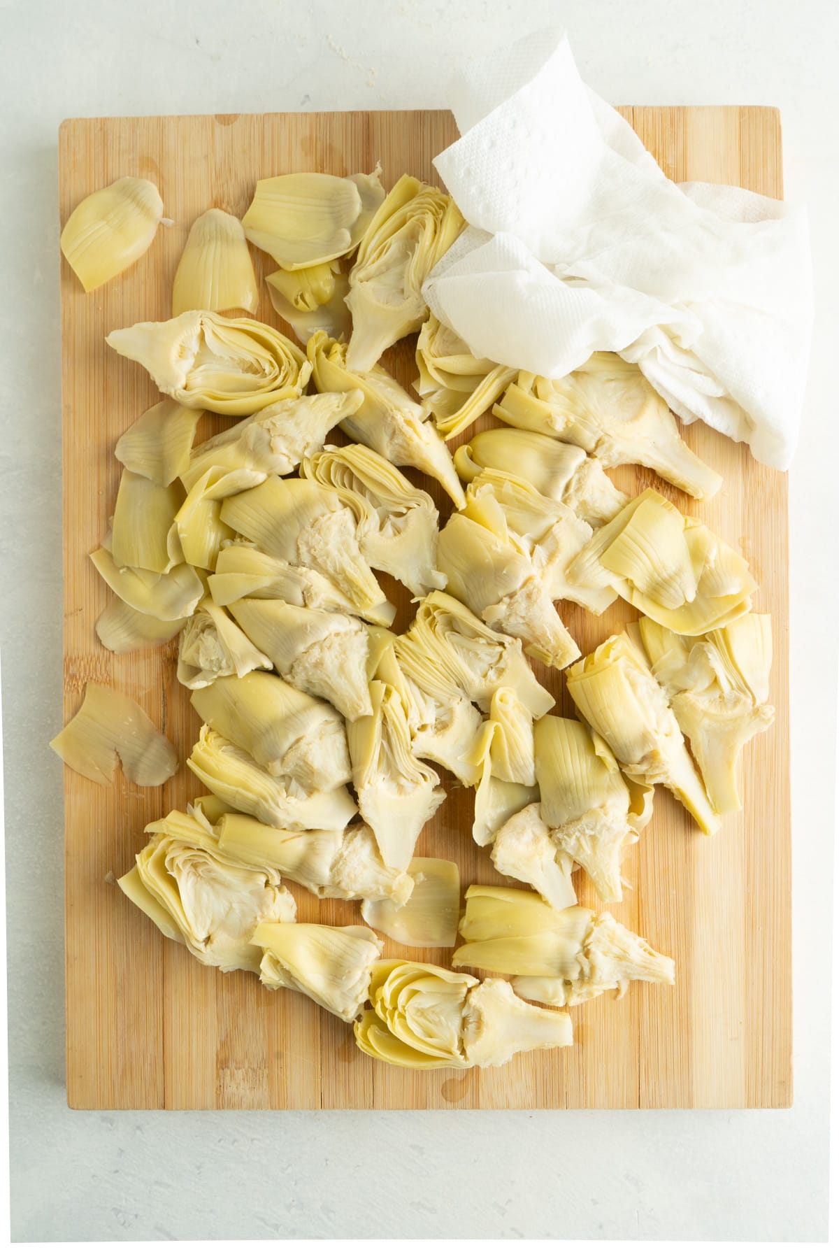 Artichoke hearts on a cutting board being dried with a paper towel.