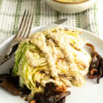 A grilled wedge salad on a plate with dressing and mushroom bacon.