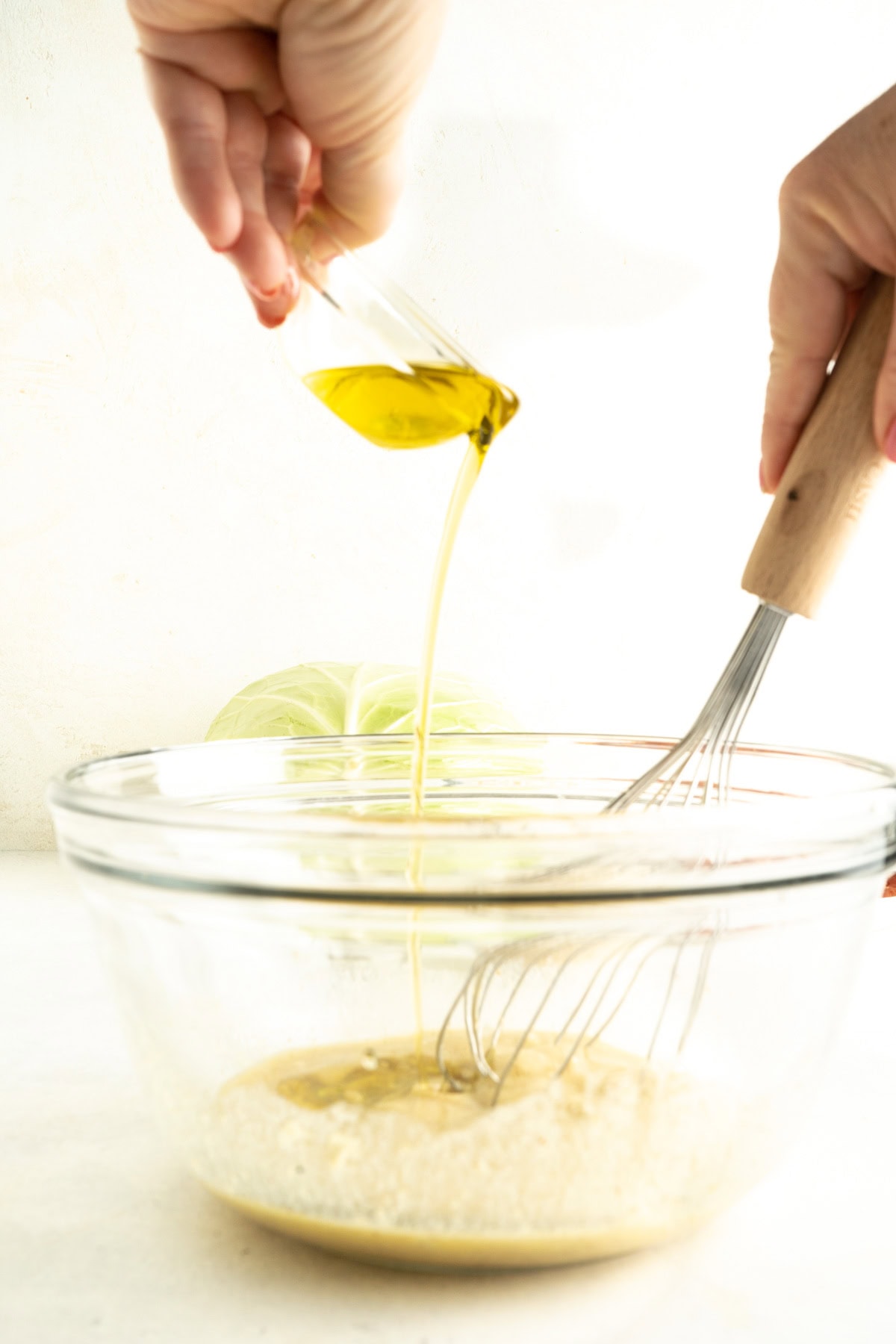 Oil being poured into a bowl while being whisked.