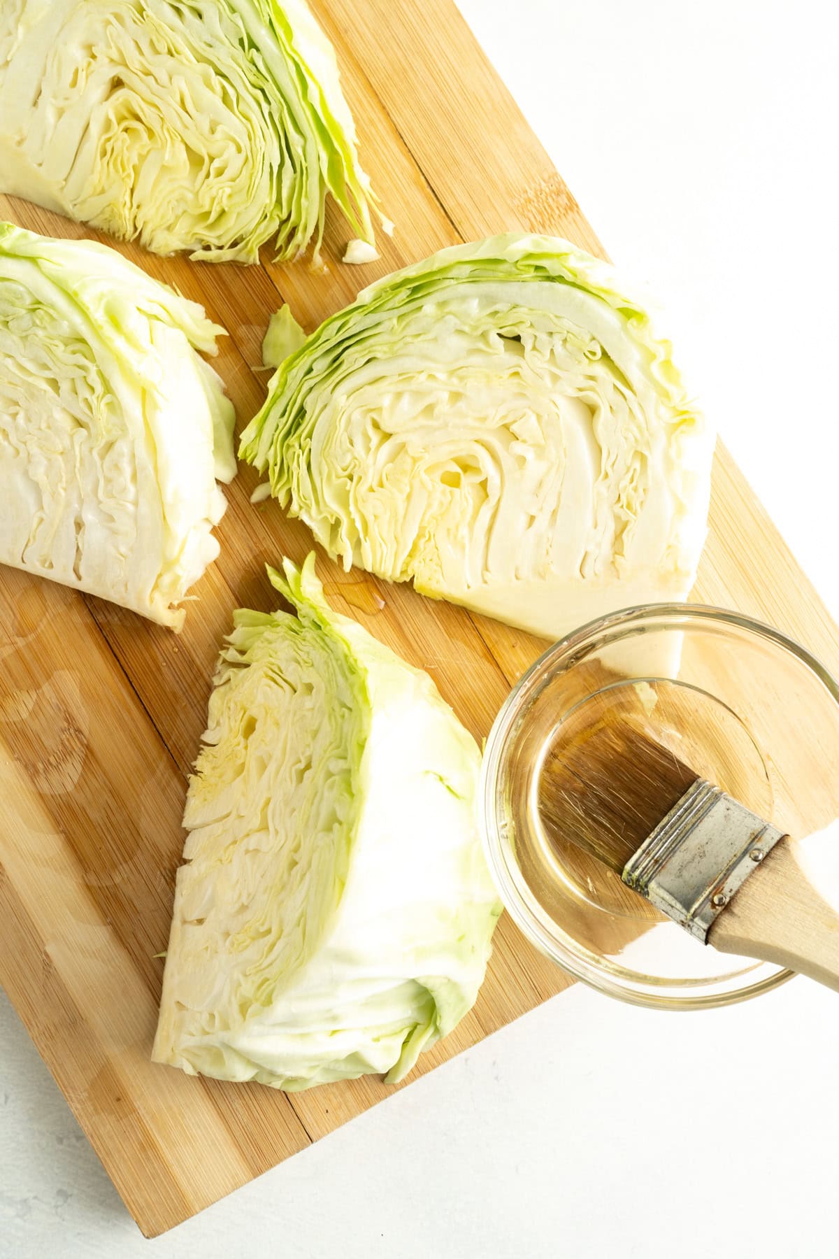 Cabbage cut into quarters and being brushed with oil.