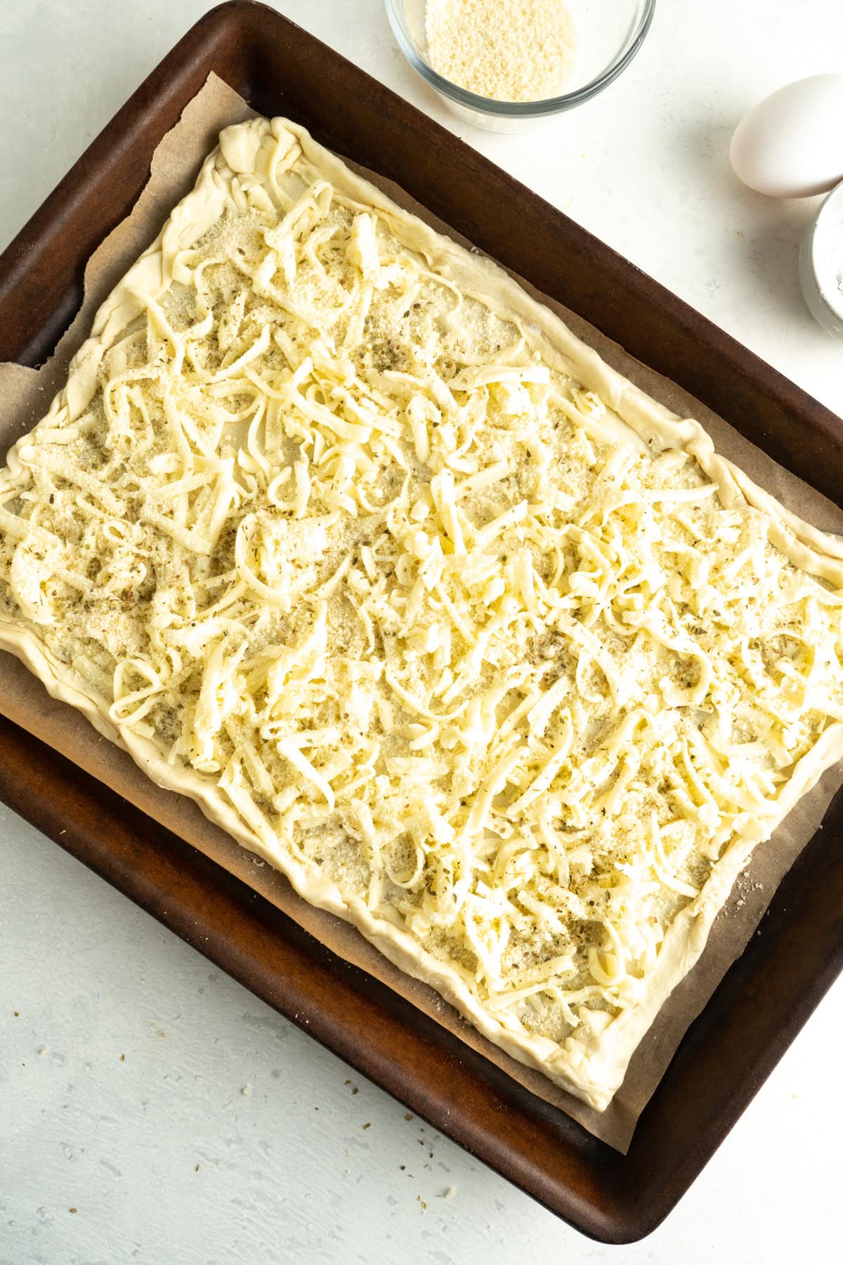 A puff pastry tart unbaked and being topped with shredded mozzarella.