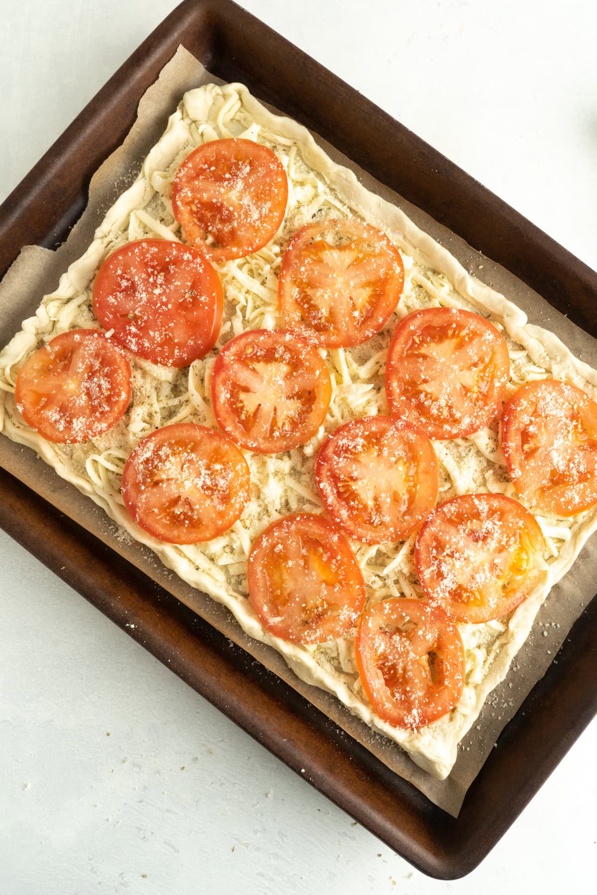 An unbaked puff pastry tomato tart on a baking sheet.