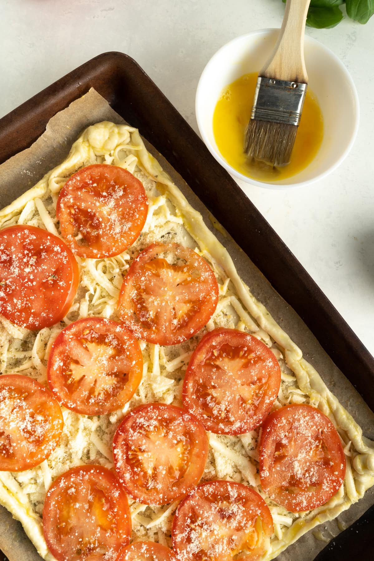 A tomato tart recipe unbaked on a table being basted with an egg wash.