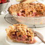 A slice of strawberry rhubarb pie with a crumble top on a table.