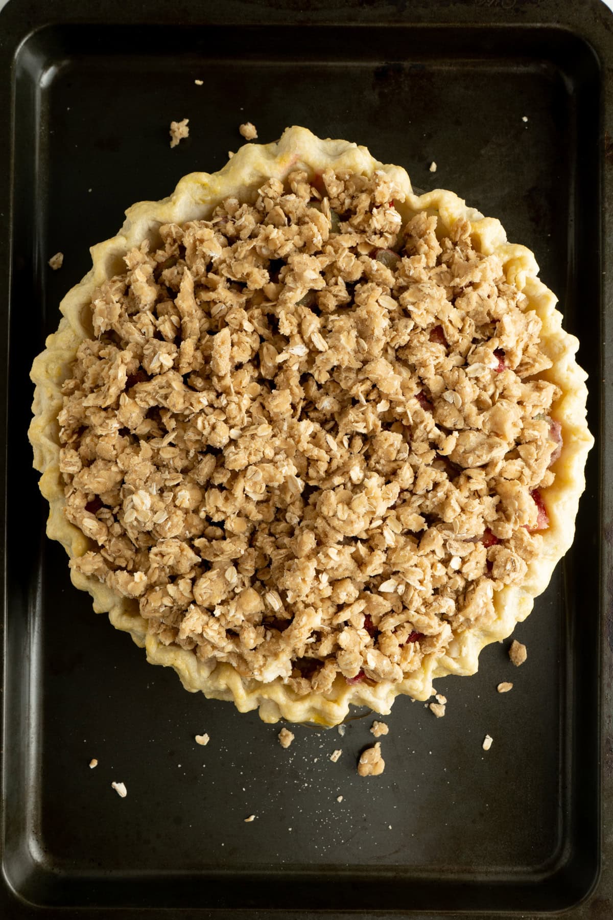 An unbaked strawberry rhubarb pie with crumble topping on a baking sheet.