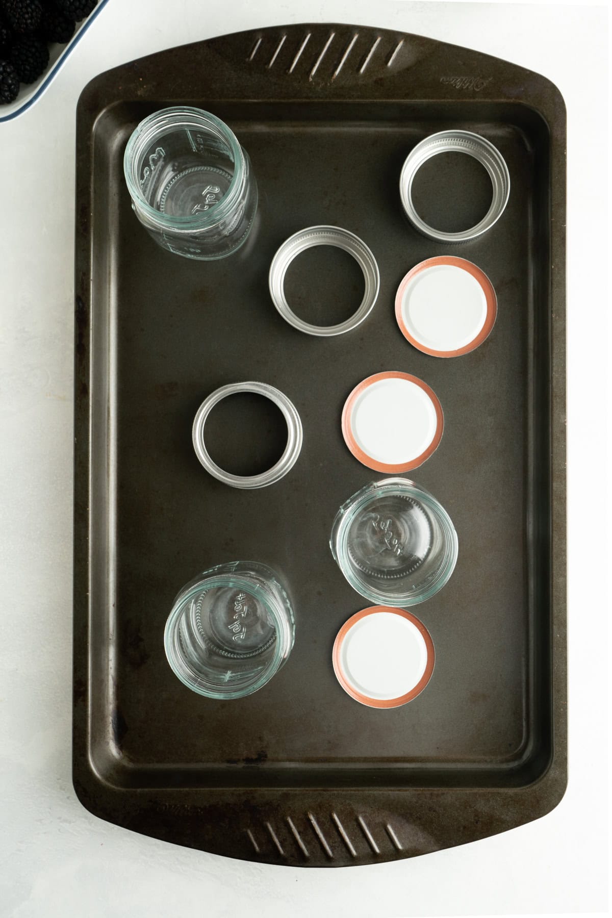 A baking sheet with glass preserve jars and lids ready to be sanitized in the oven.