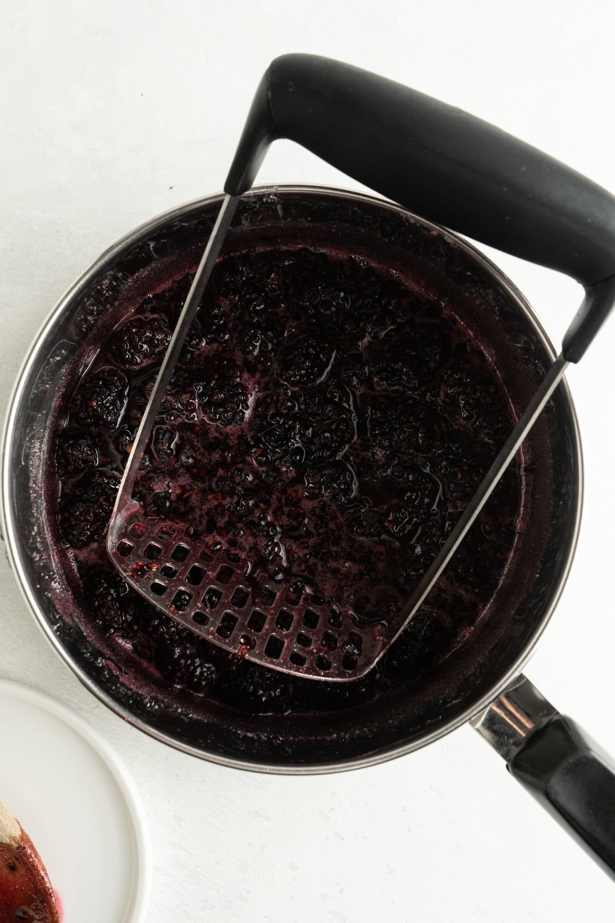 Cooked blackberries being mashed in a pot for a blackberry jam recipe.