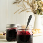 Two jars of easy blackberry jam on a table with flowers.
