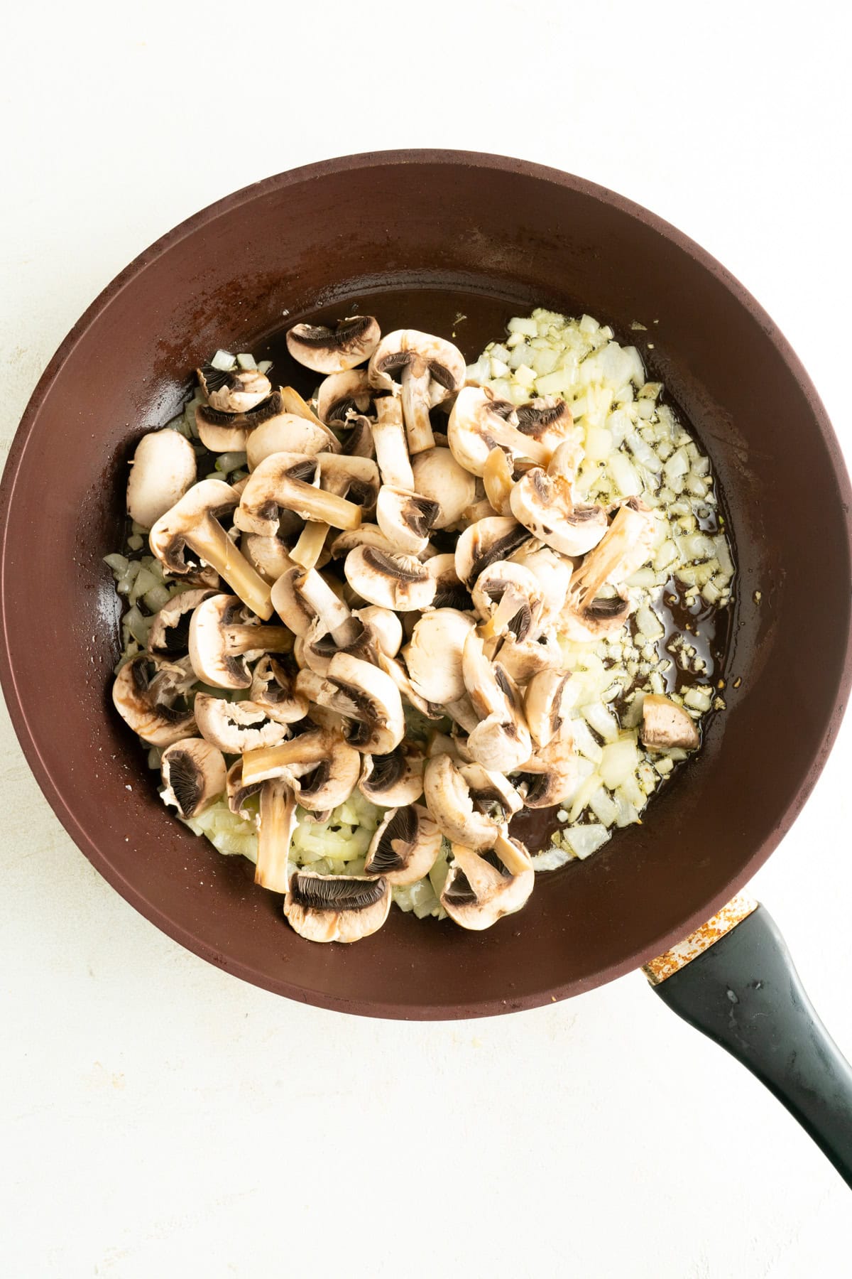 Sliced mushrooms and onions in a pan.