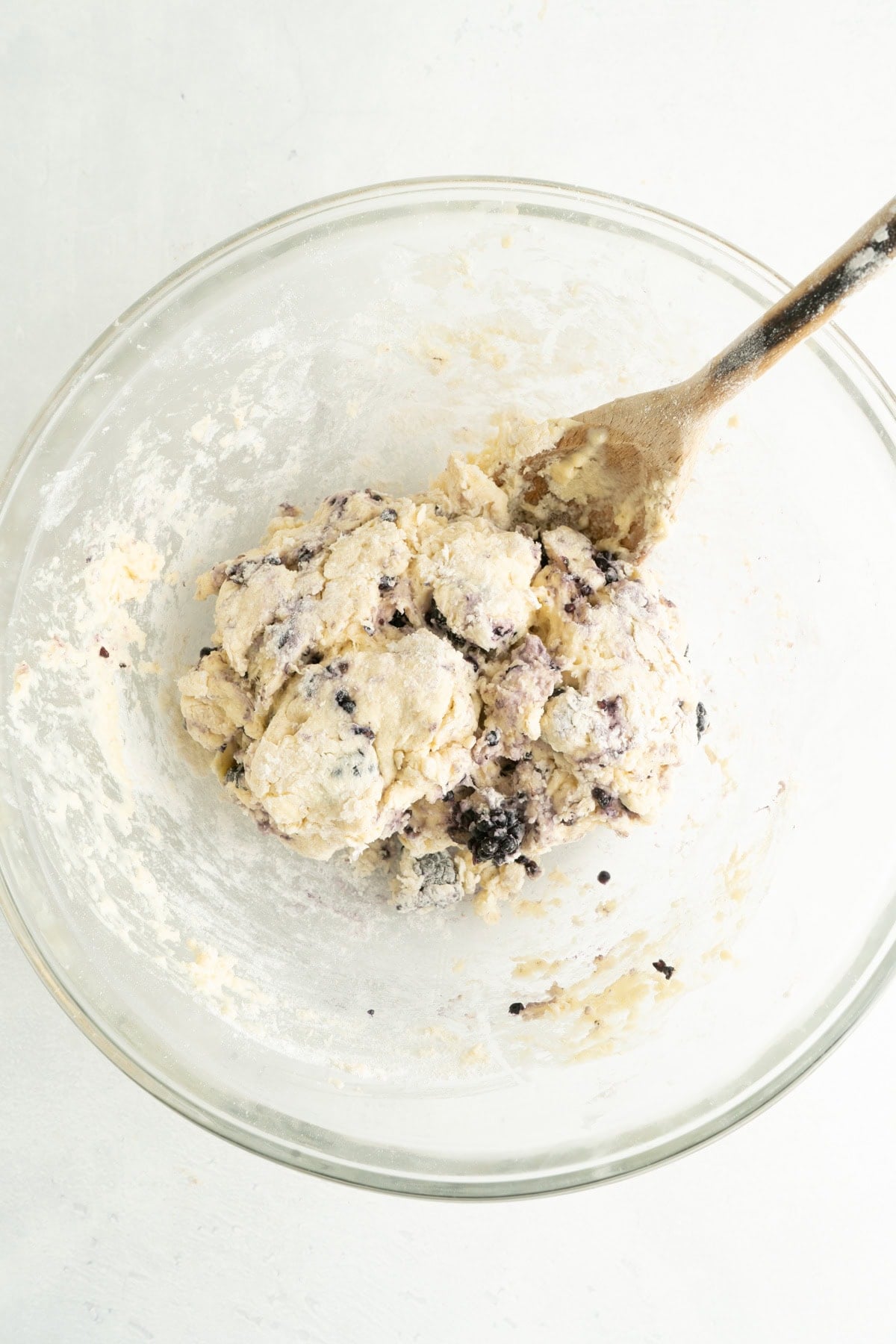 Buttermilk scone batter with blackberries in a bowl with a wooden spoon.