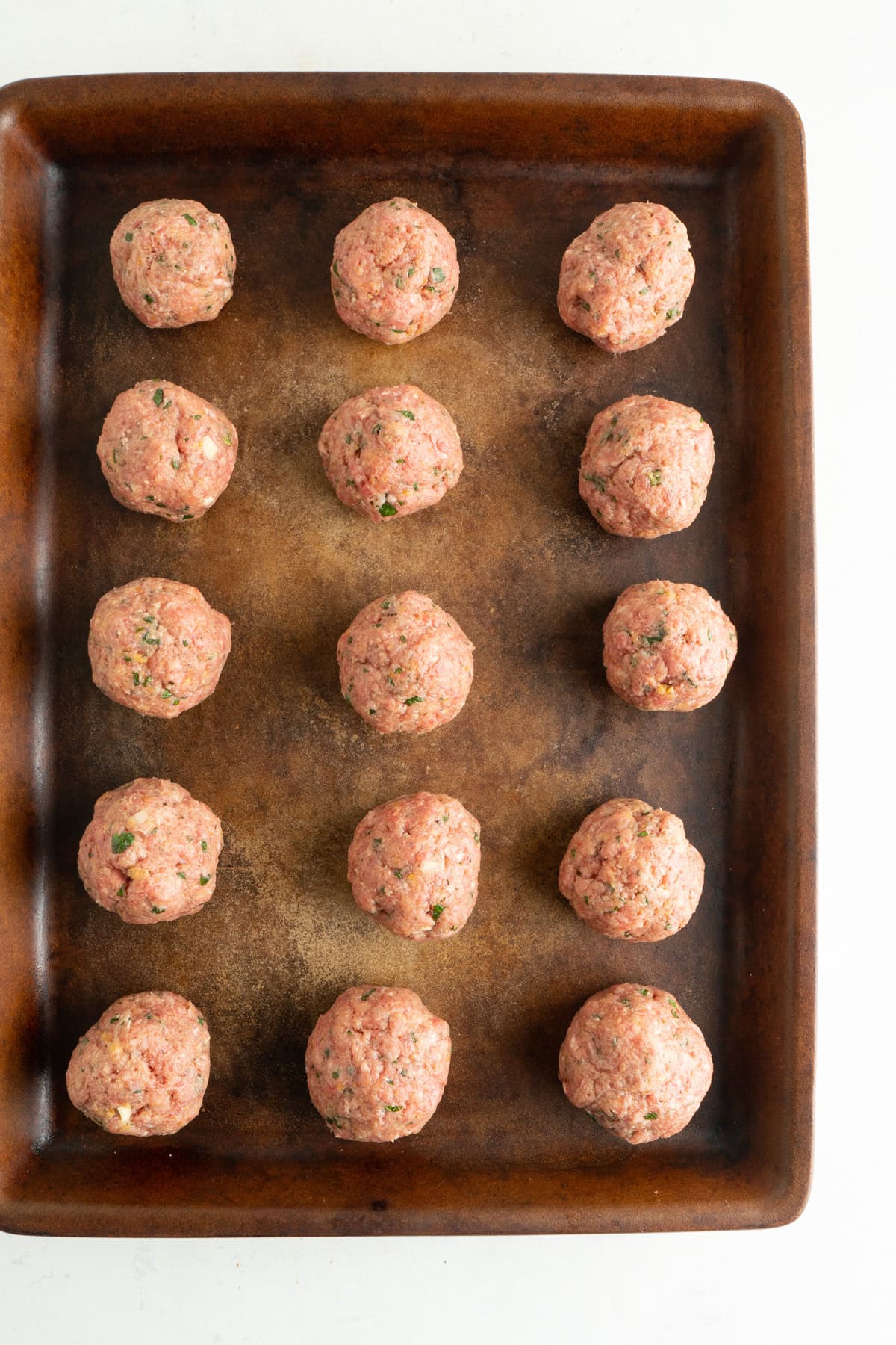 A recipe for Italian meatballs rolled into balls and placed on a baking sheet to be baked.