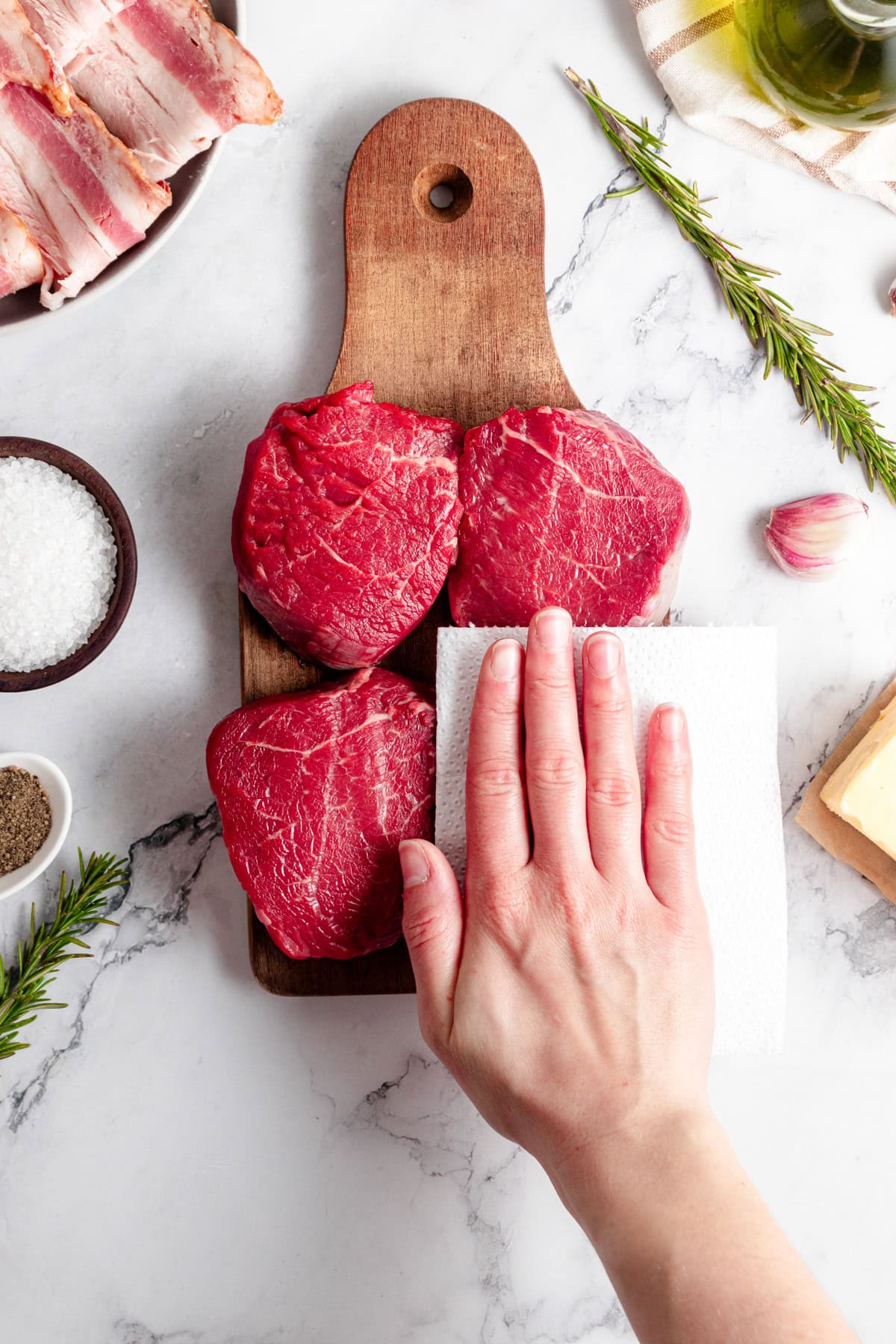 Filet mignon steaks being patted dry with a paper towel.