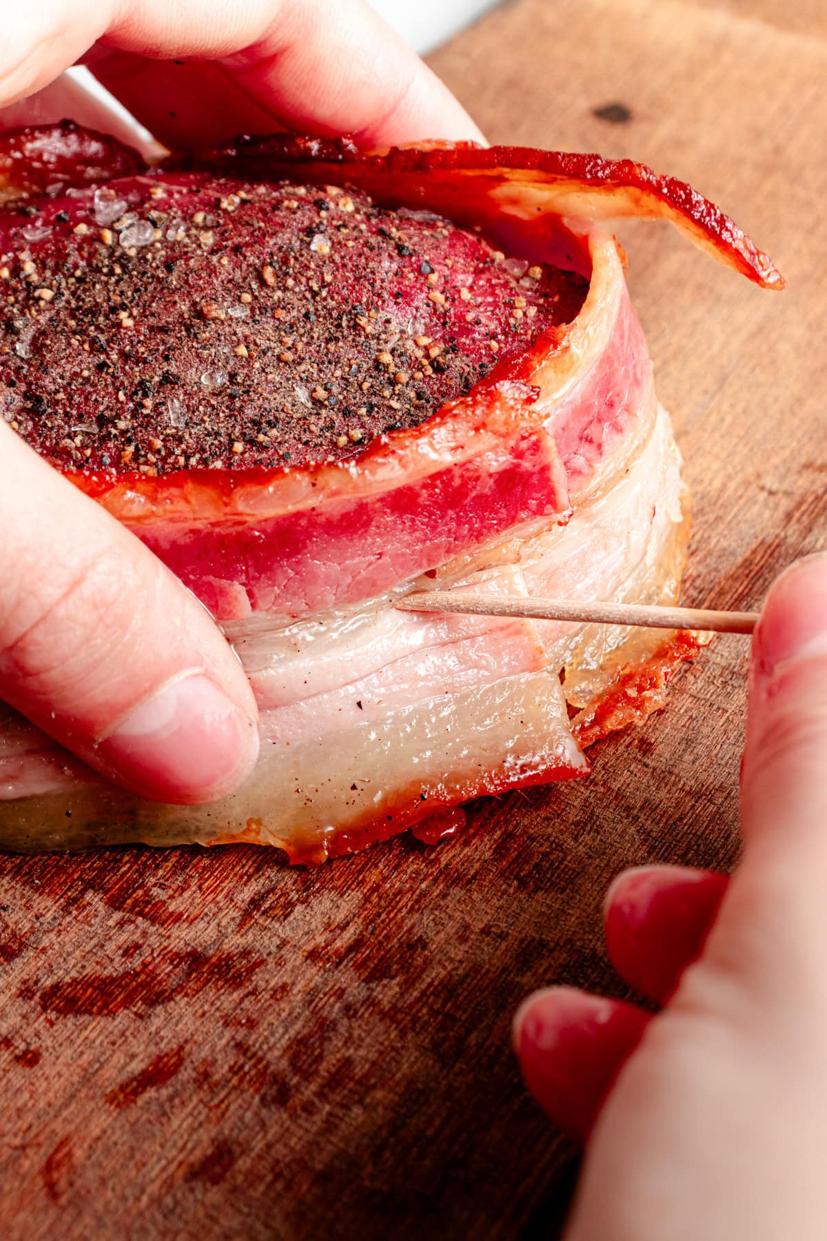 A filet mignon being wrapped and bacon and secured with a toothpick.