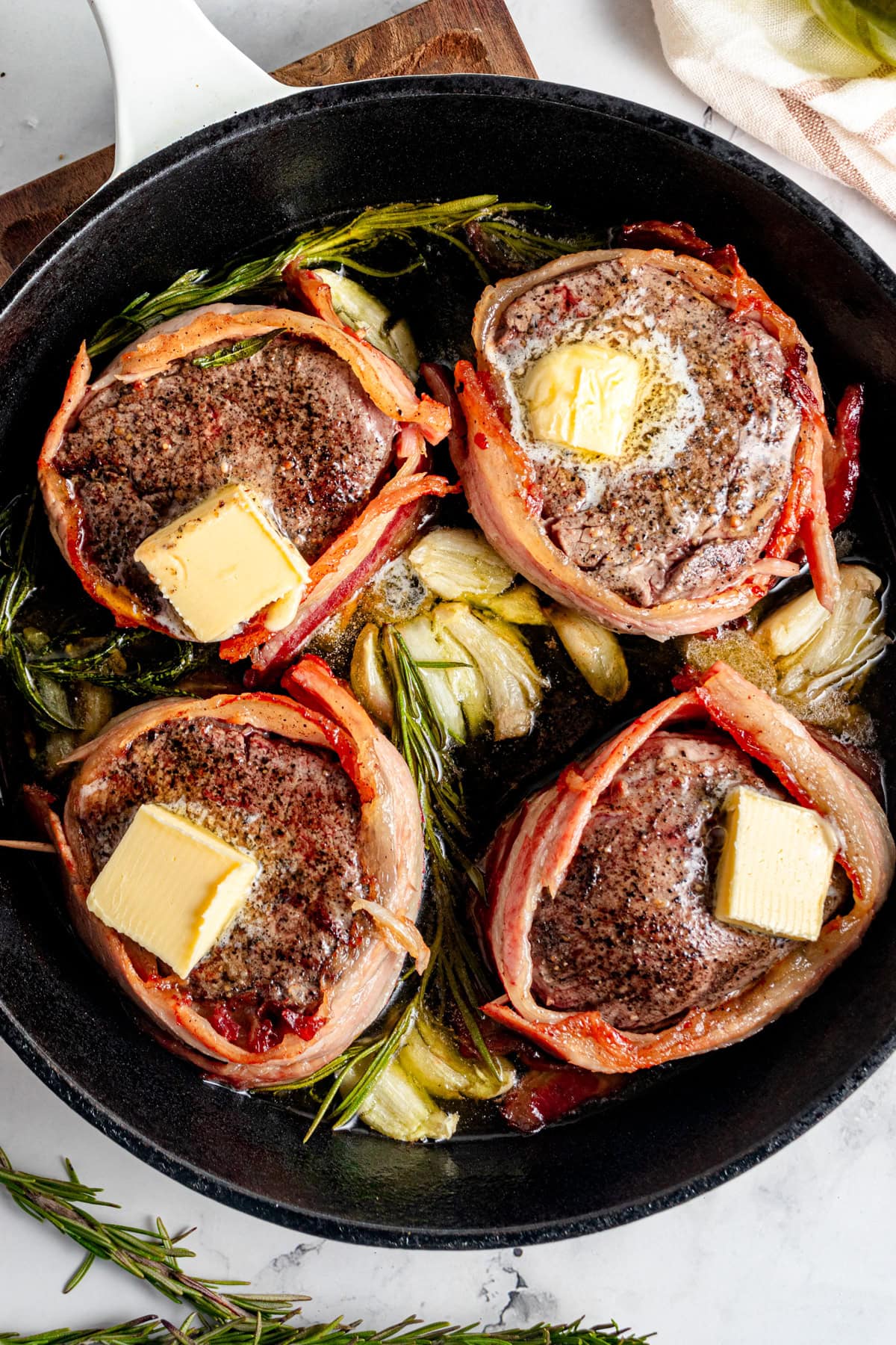 Bacon wrapped filet mignon steaks in a cast iron pan with garlic, butter and rosemary.