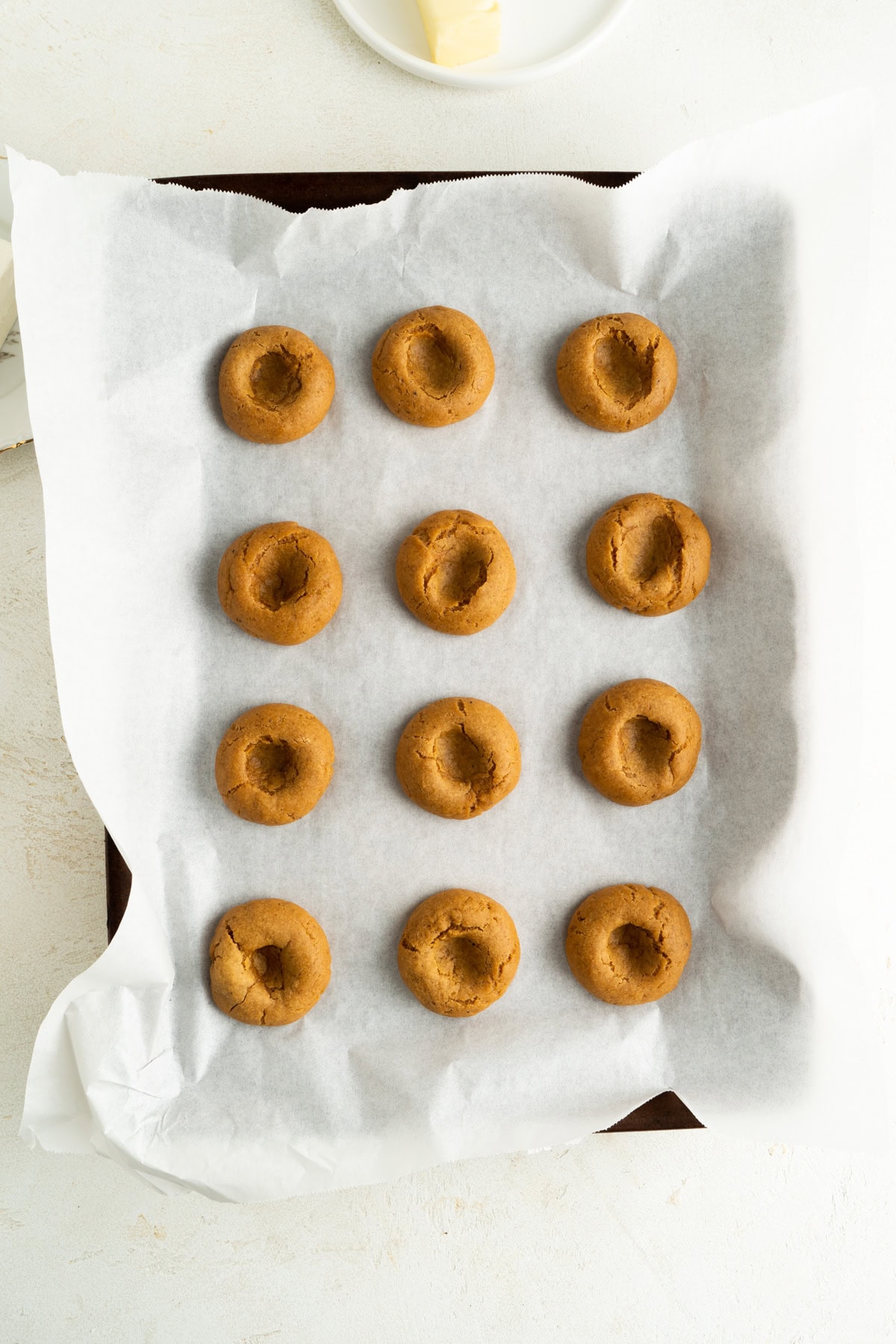 A pumpkin cheesecake cookies recipe on a baking sheet with holes pushed in for cream cheese.