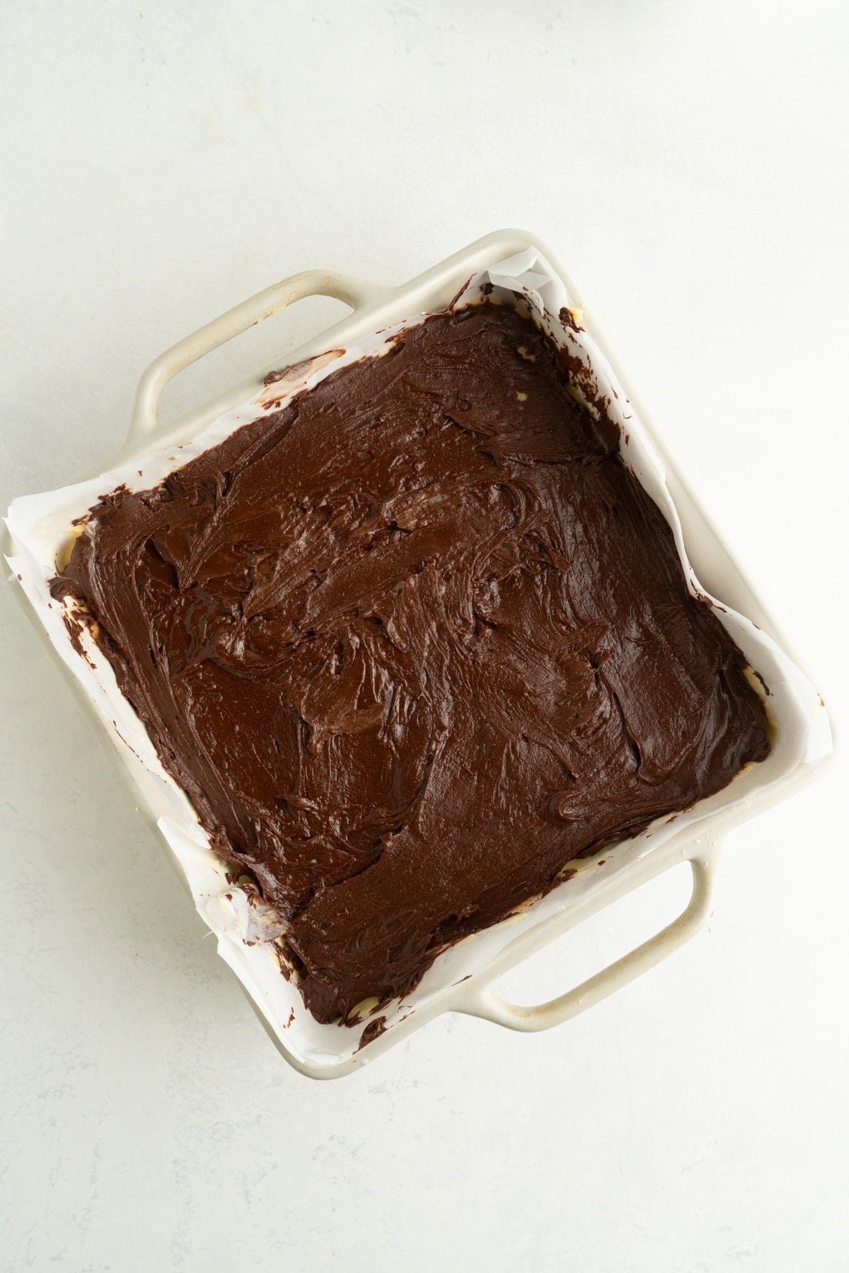 A square pan with a chocolate layer added to a recipe for Nanaimo Bars.