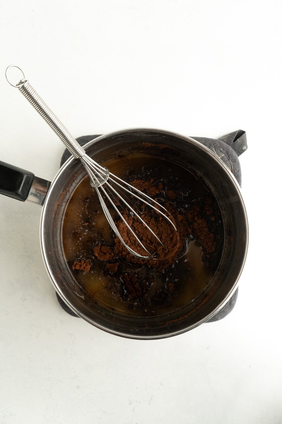 A pot with cocoa powder being whisked into melted butter.