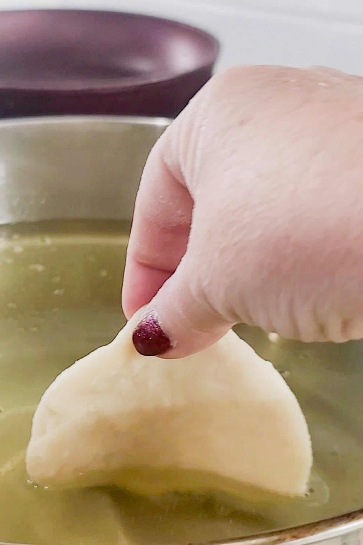 Adding the uncooked johnny cake to a pot of hot oil.