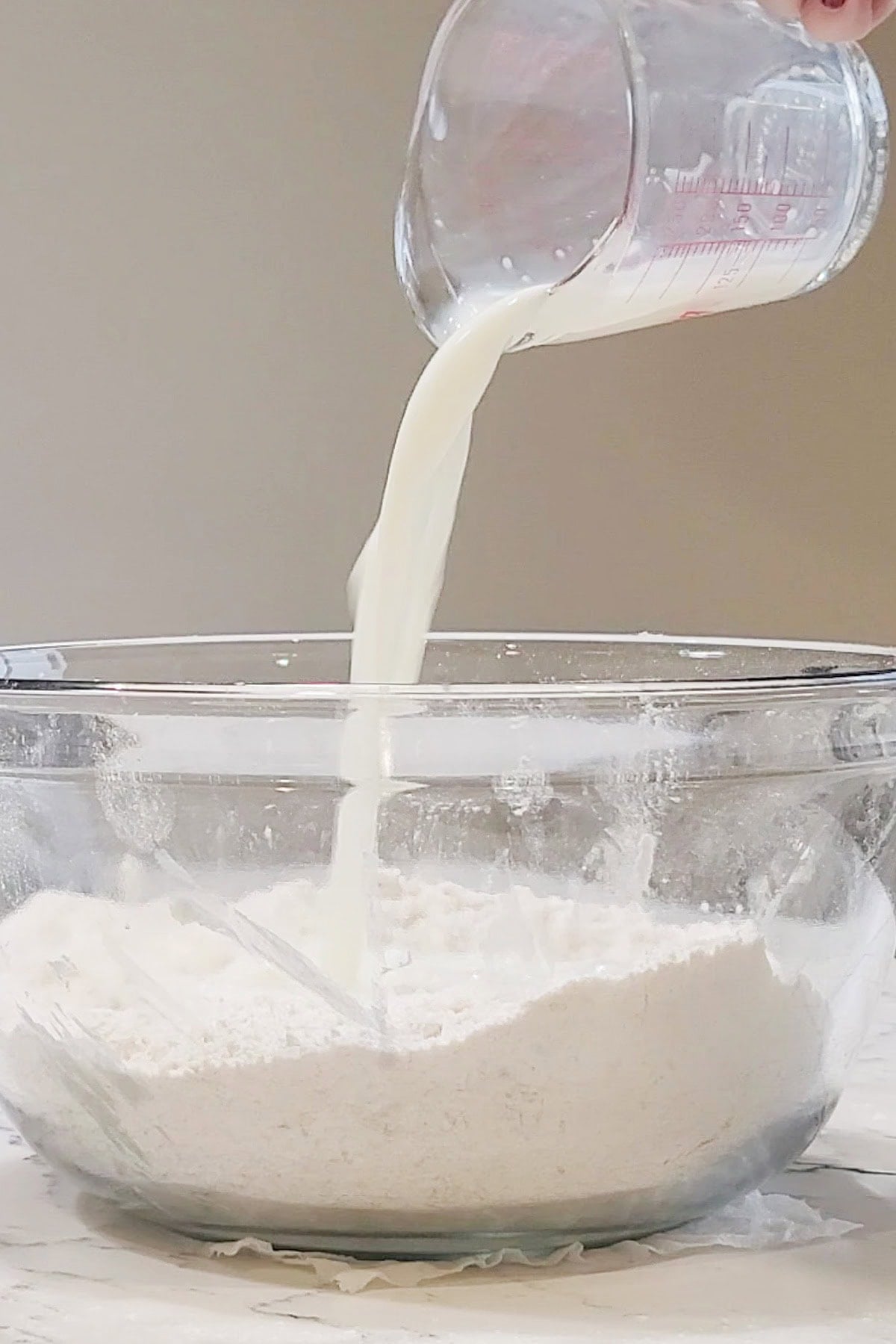 A large bowl of flour with milk being poured in.