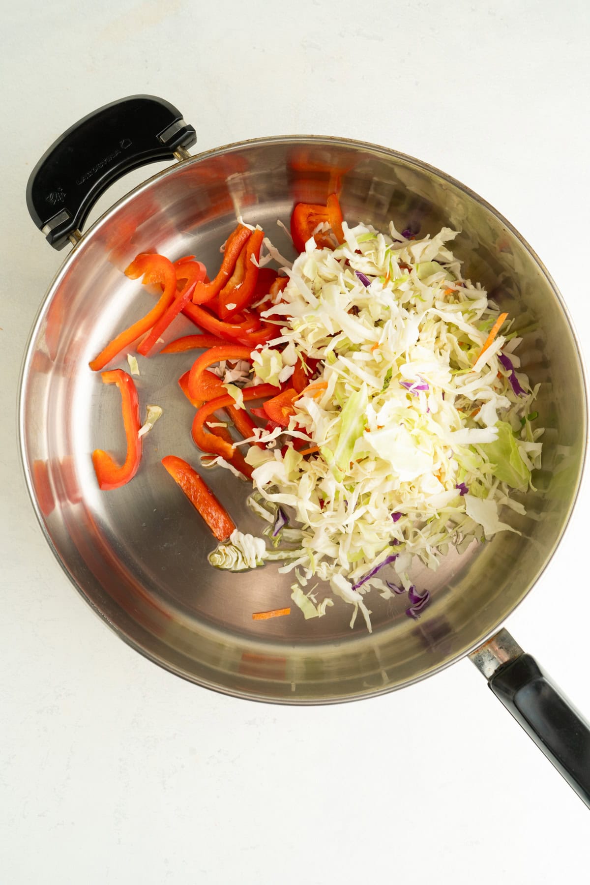 A large pan with sliced red peppers and coleslaw mix.